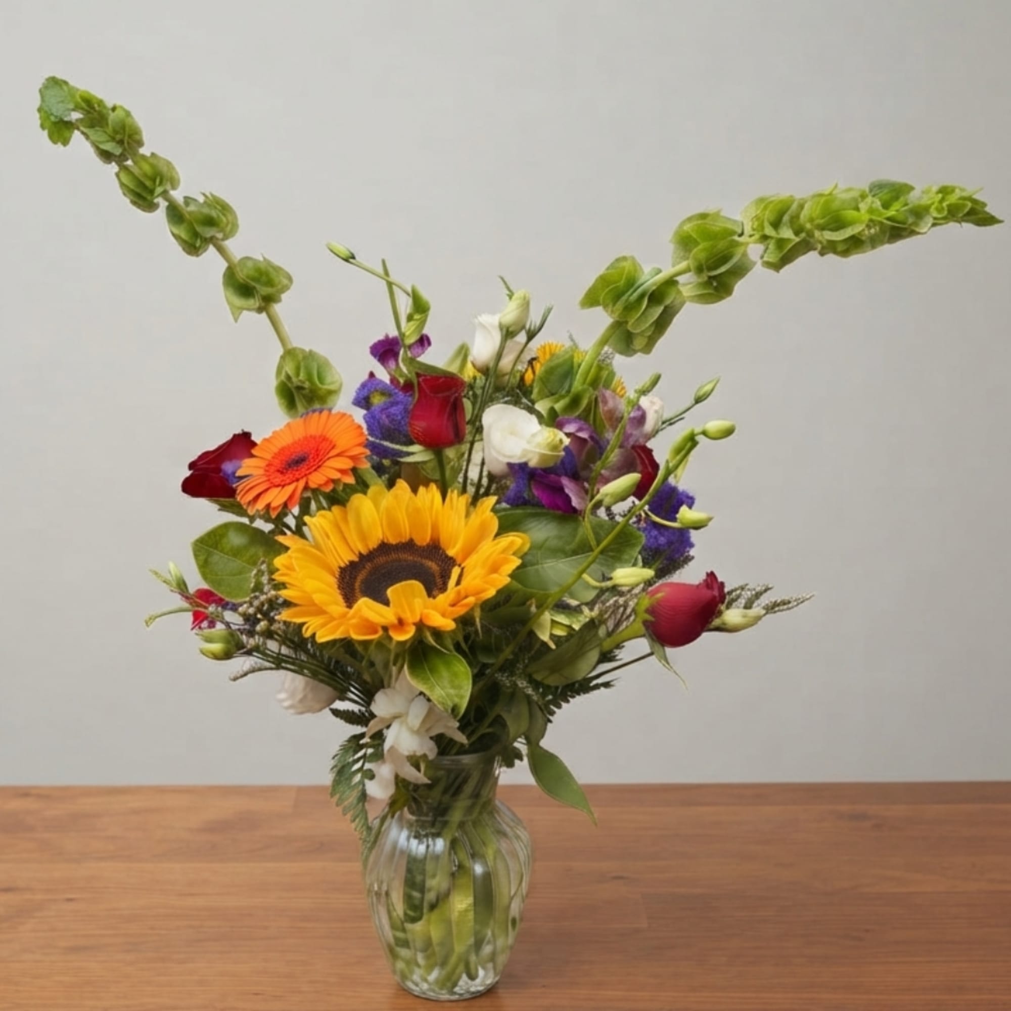 Mixed bouquet with sunflowers, roses, and orchids in a glass vase
