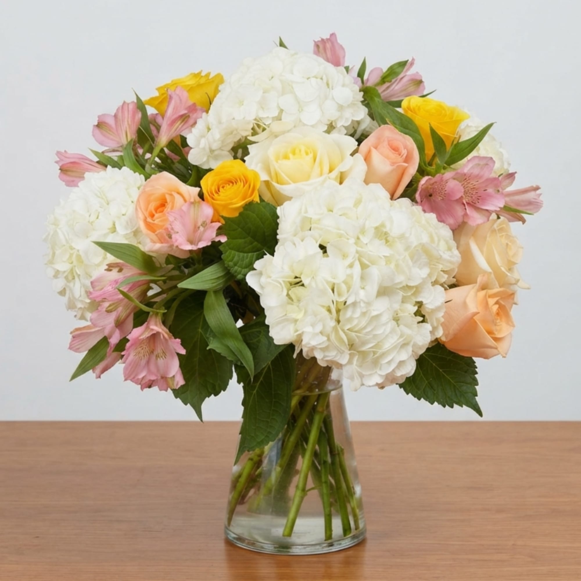 Mixed bouquet of white hydrangeas, roses, and pink flowers in a clear glass vase