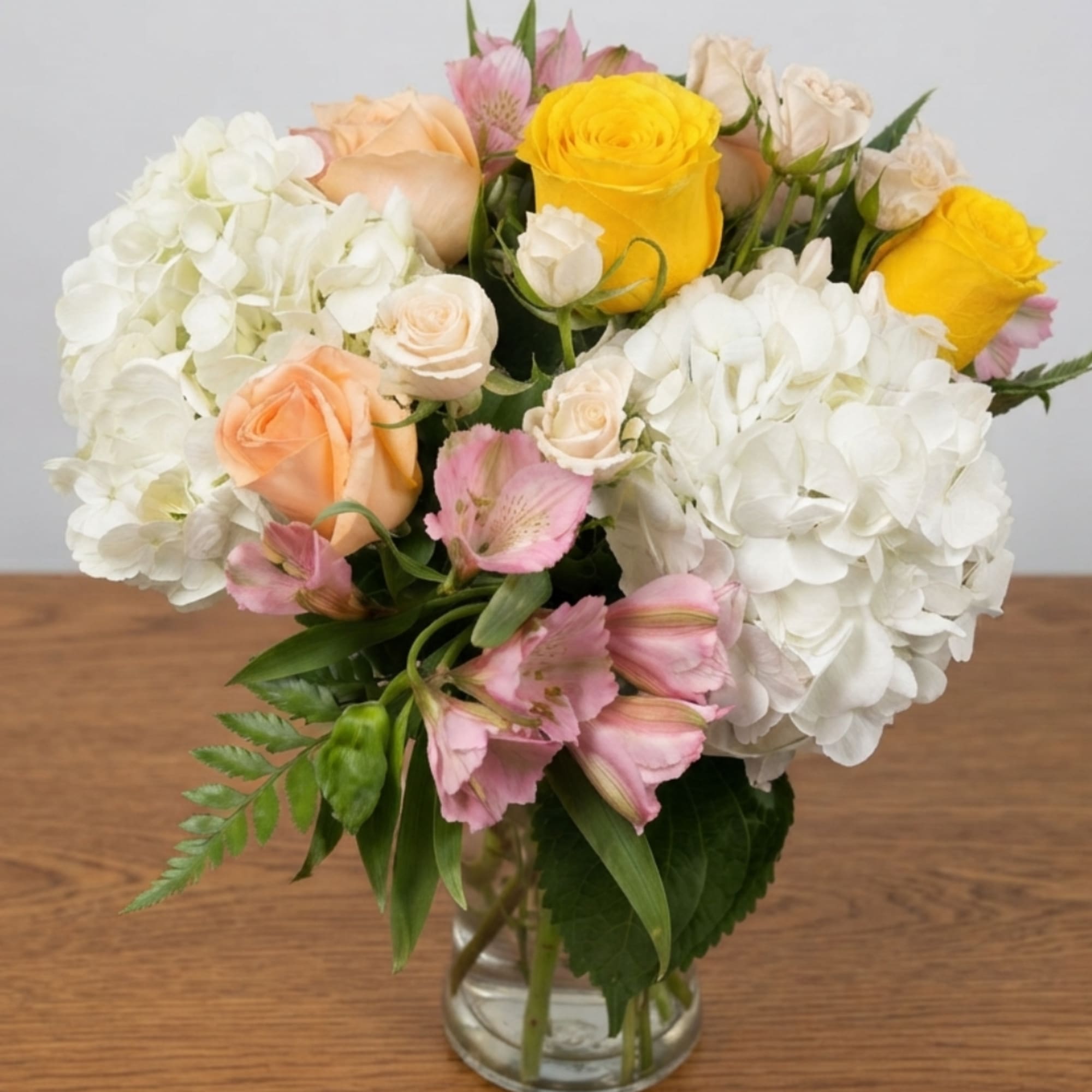 Bouquet of yellow, peach, and white roses with pink alstroemeria in a glass vase