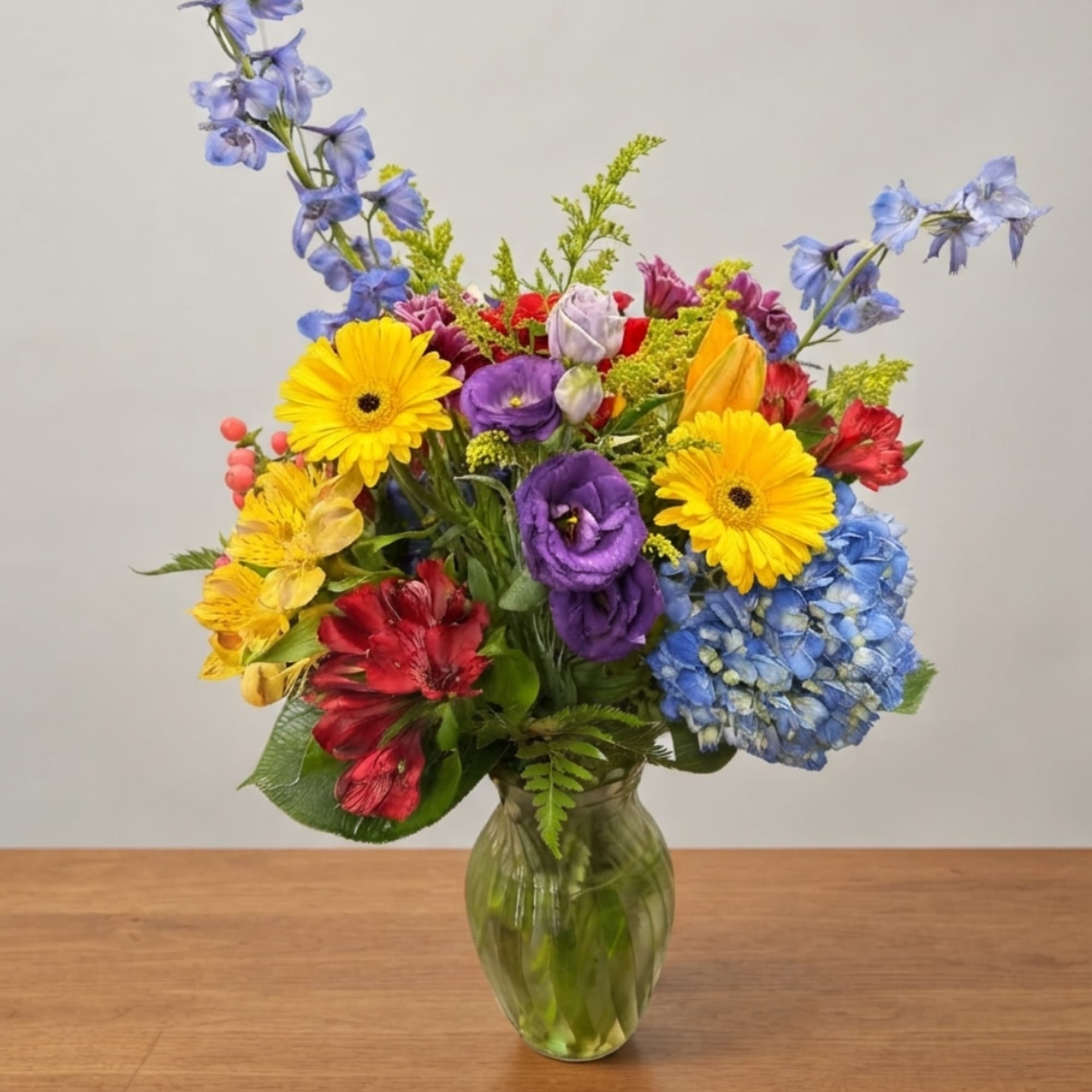 Colorful mixed bouquet in a green glass vase with blue, yellow, red, and purple flowers