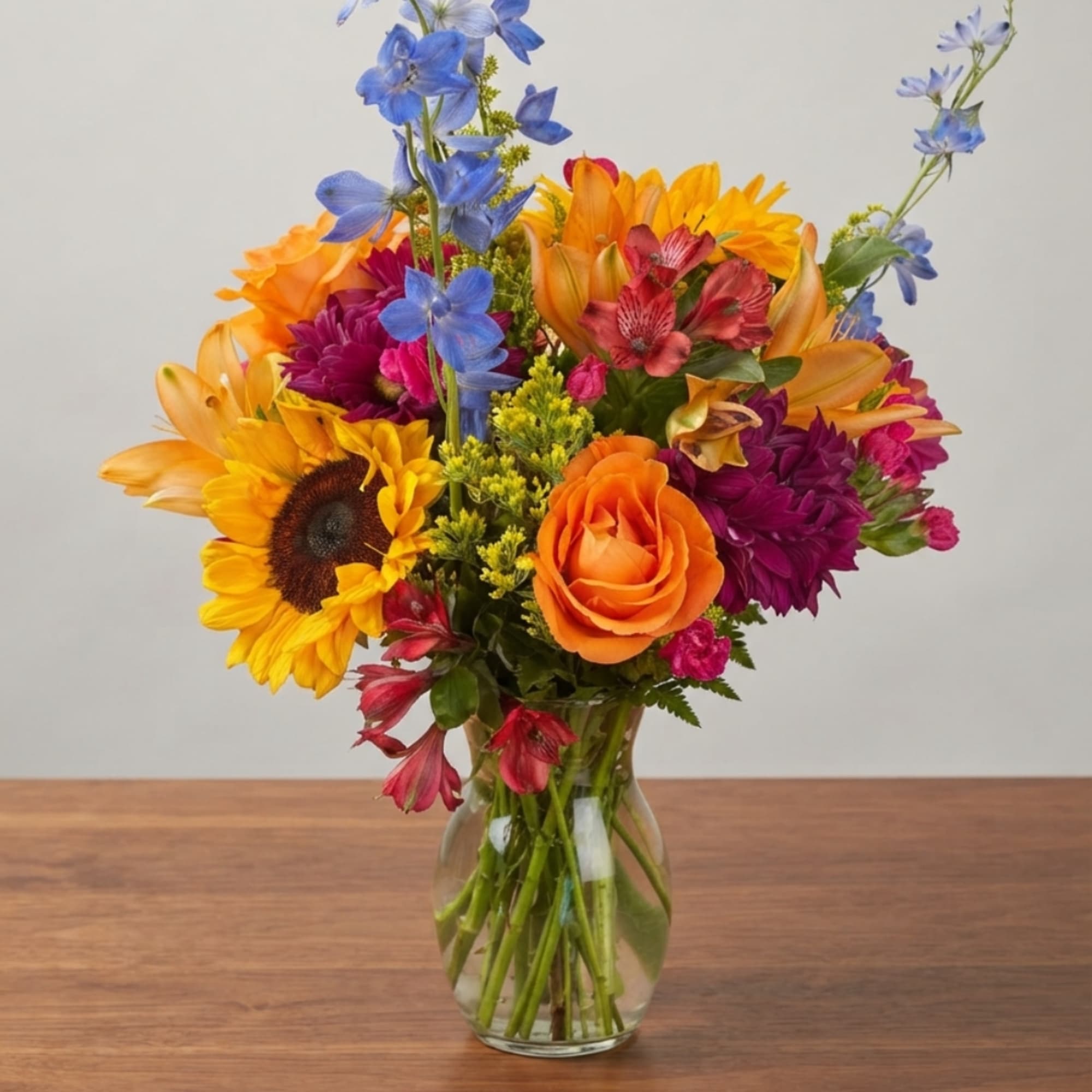 Colorful mixed bouquet in a clear glass vase with sunflowers and roses