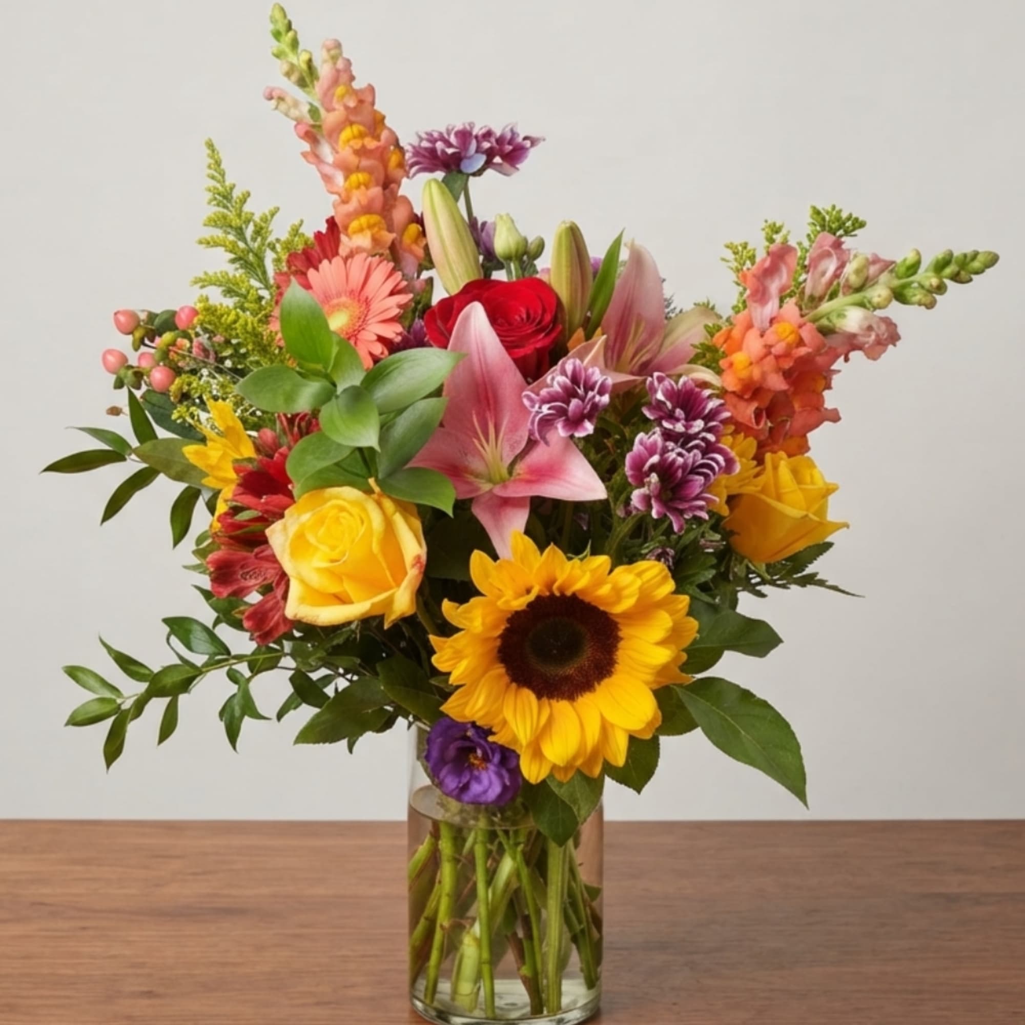 Colorful mixed bouquet in a clear glass vase with roses, lilies, sunflower, and snapdragons
