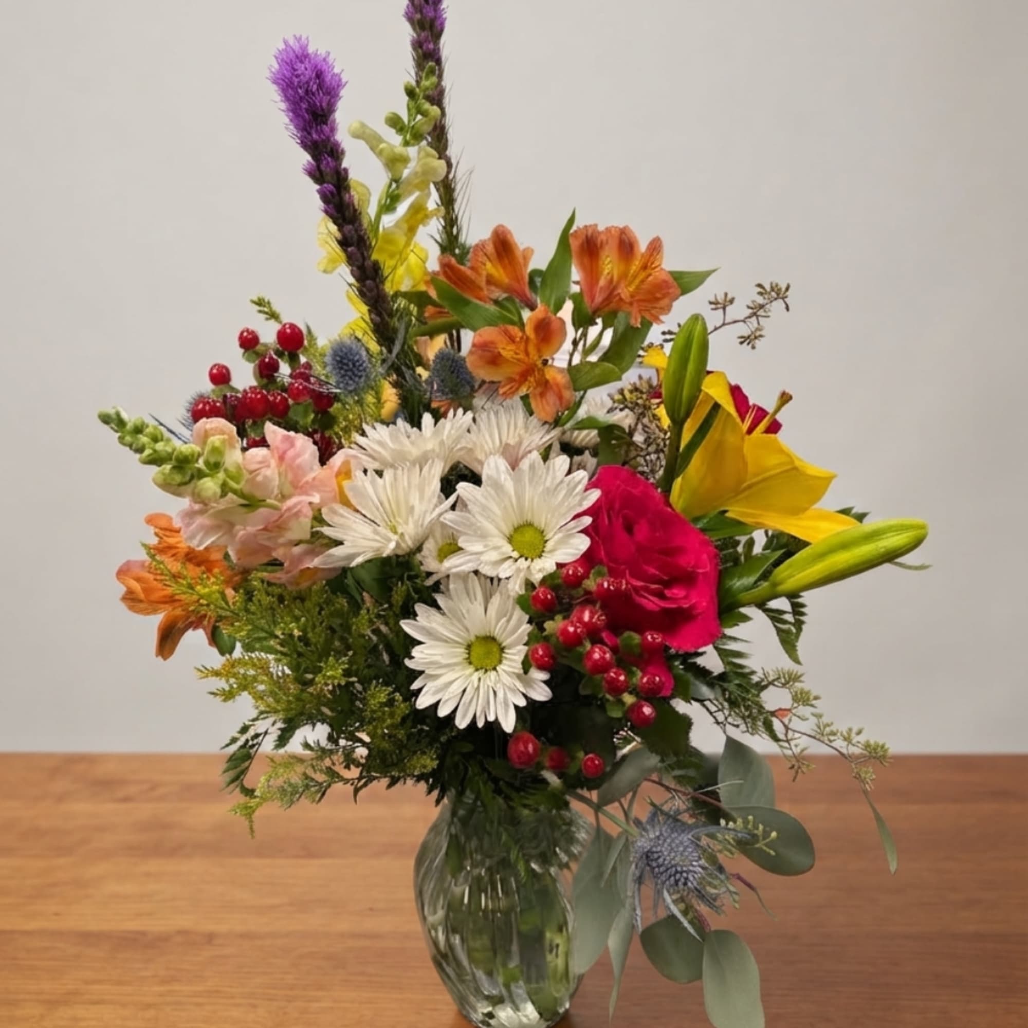 Mixed bouquet in a clear glass vase with white daisies, lilies, and orange blooms