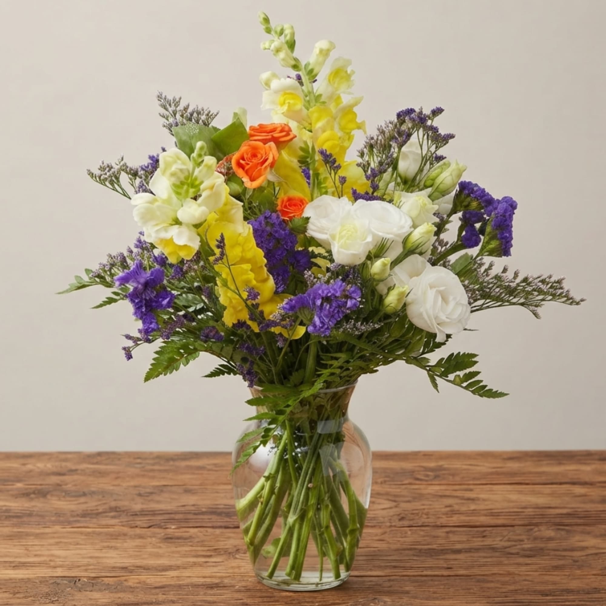 Mixed bouquet of white, yellow, orange, and purple flowers in a glass vase