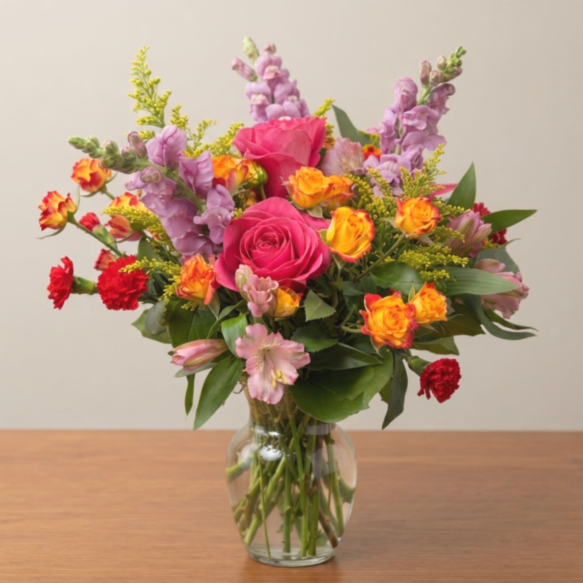 Mixed bouquet of pink roses, purple snapdragons, and orange spray roses in a glass vase