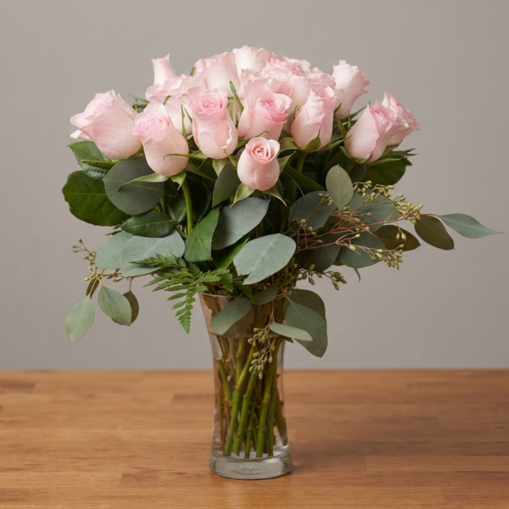 Pink roses arranged in a clear glass vase with eucalyptus foliage