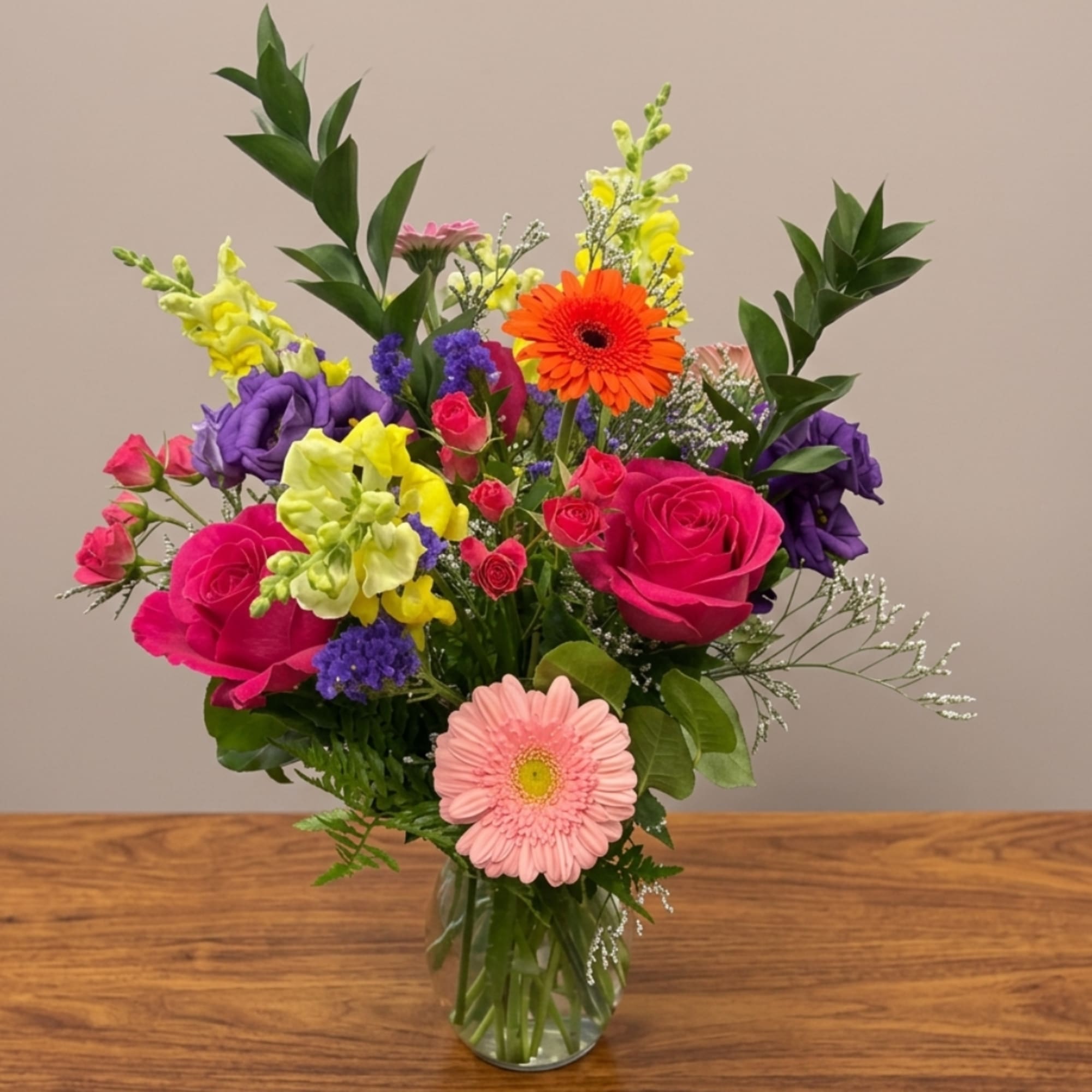 Mixed bouquet in a clear glass vase with pink, purple, yellow, and orange flowers