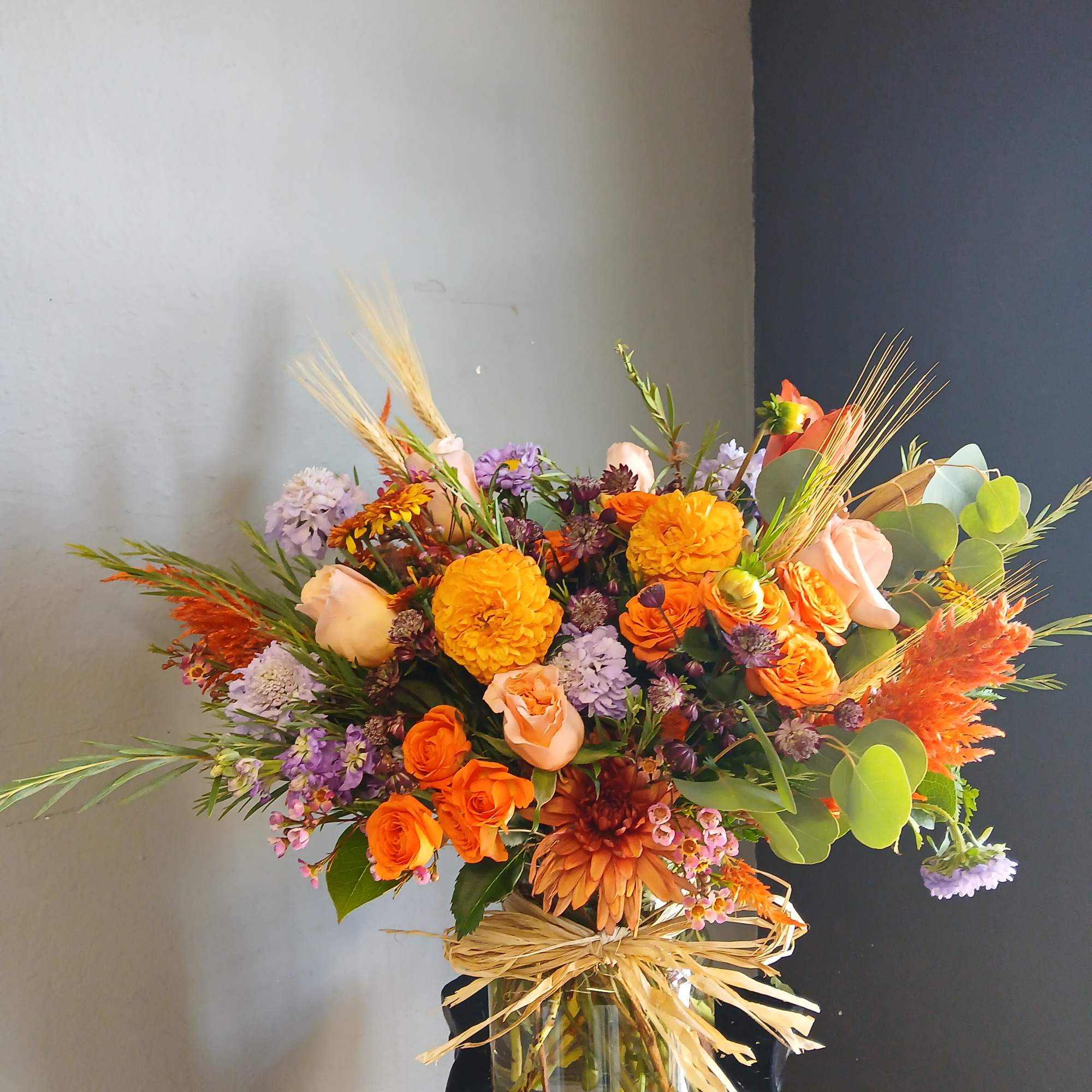 Orange and lavender mixed bouquet in a glass vase with raffia bow