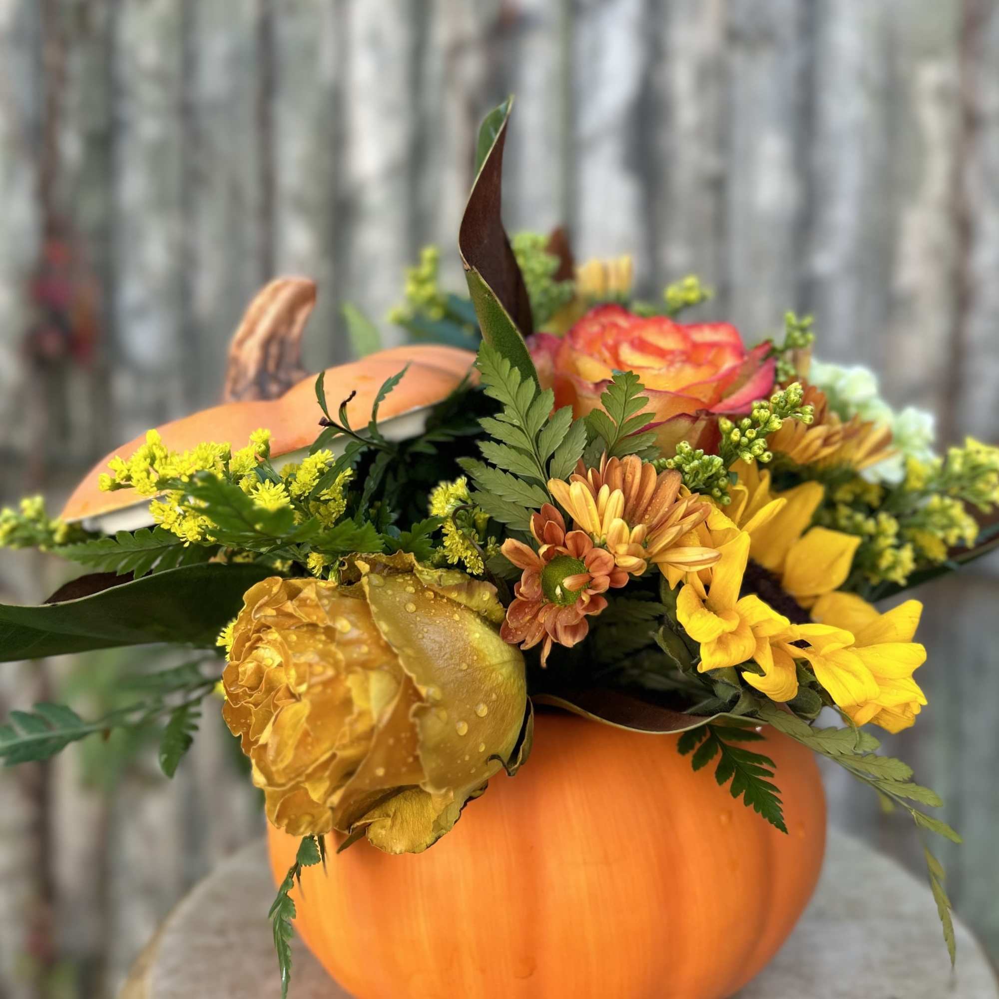 Fall flower arrangement in a pumpkin container with yellow and orange blooms