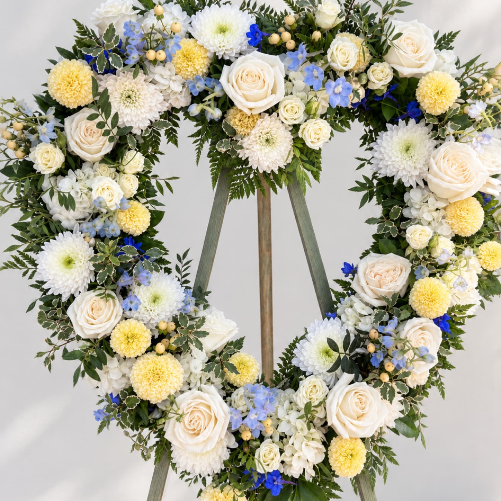 Heart-shaped floral wreath with white, yellow, and blue flowers on an easel
