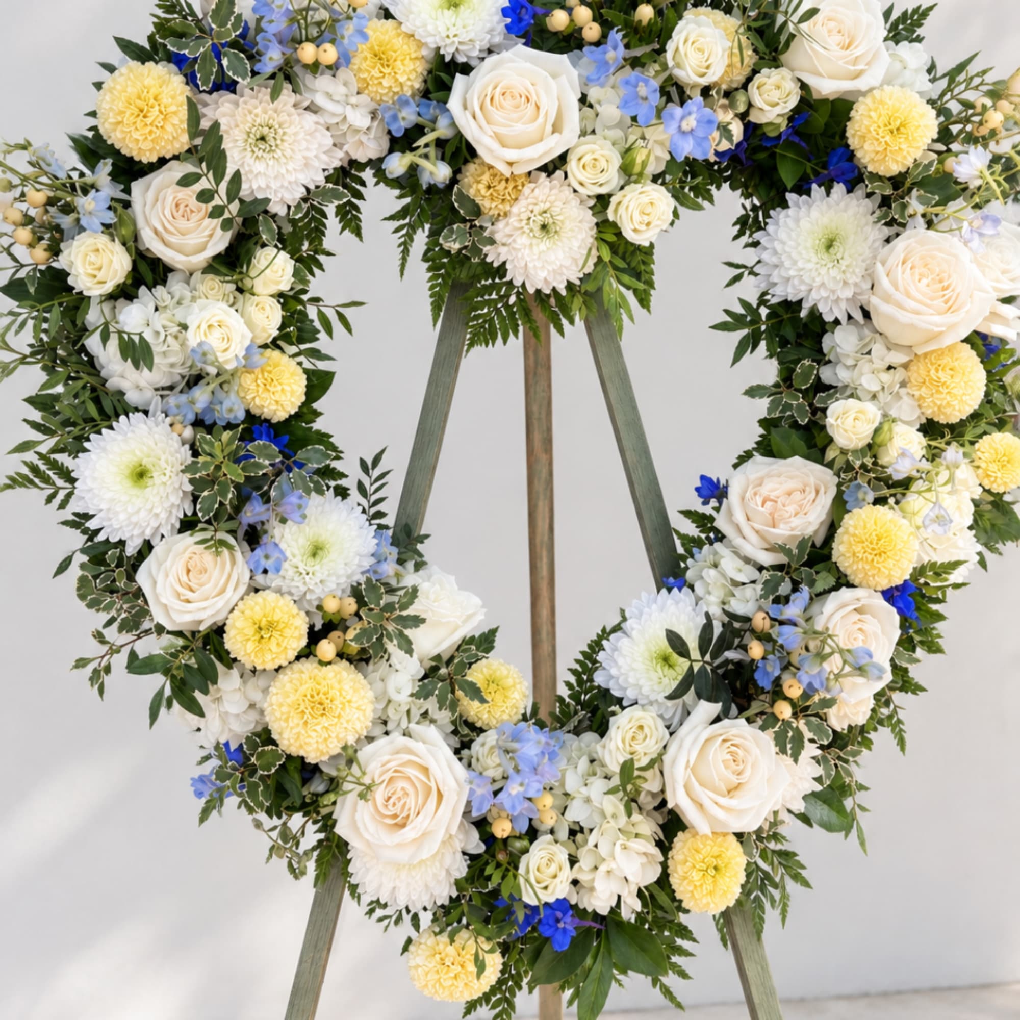 Heart-shaped floral wreath with white roses, yellow mums, and blue accents