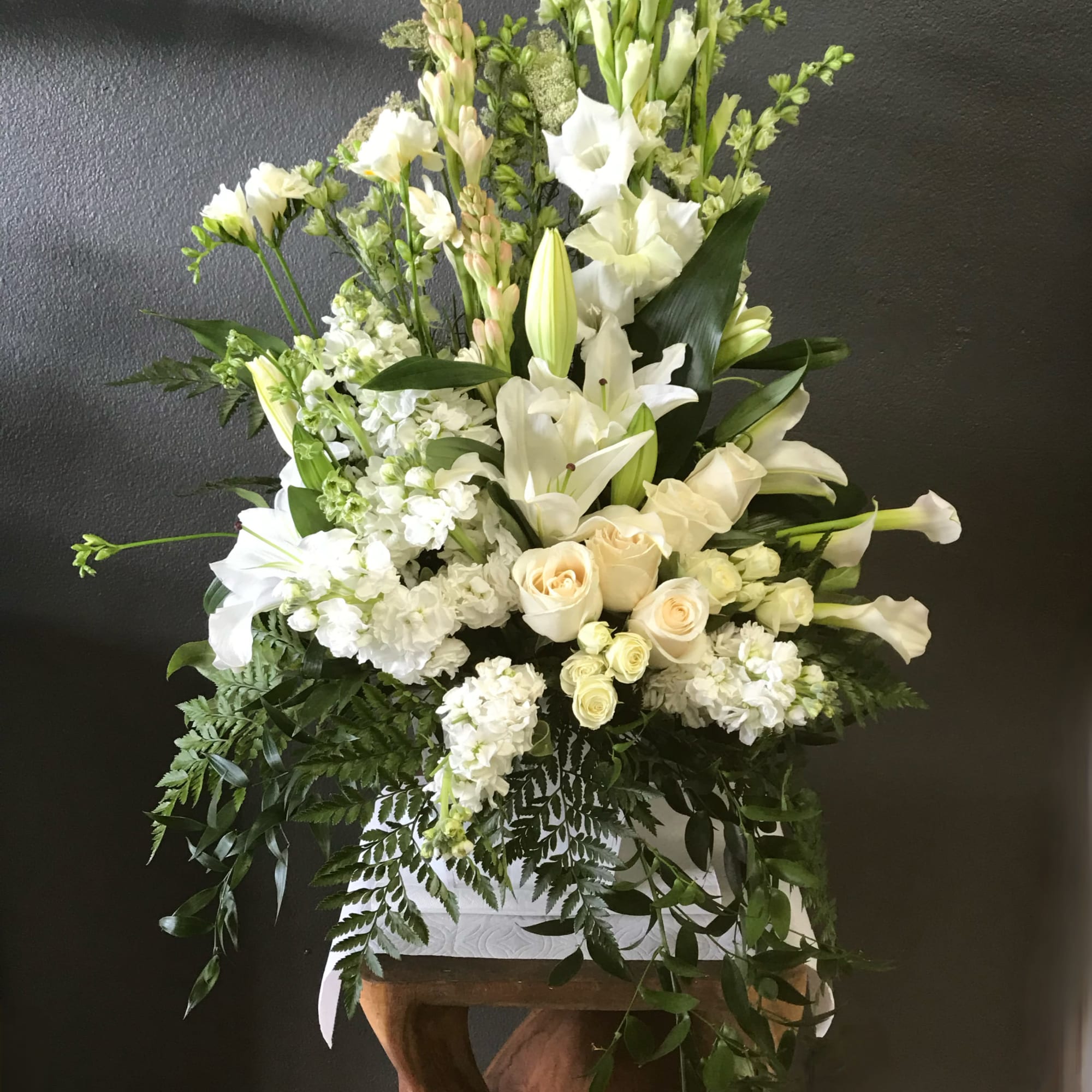 Tall white floral arrangement with lilies and roses in a white container