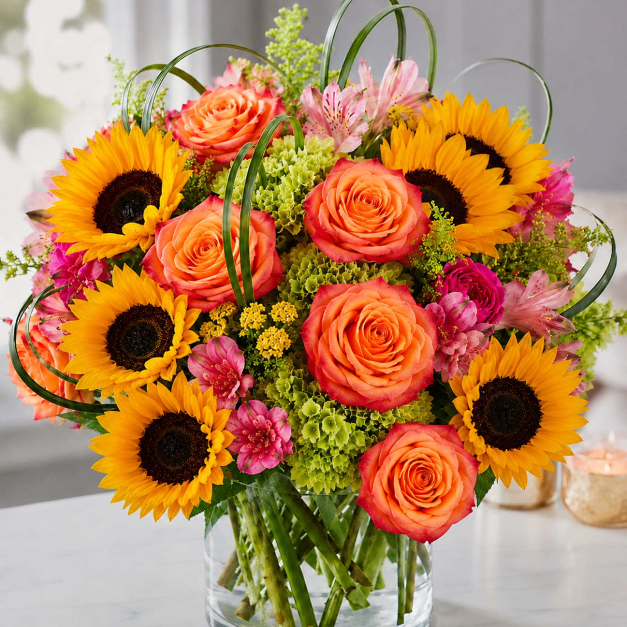 Bouquet of sunflowers, orange roses, and pink flowers in a glass vase