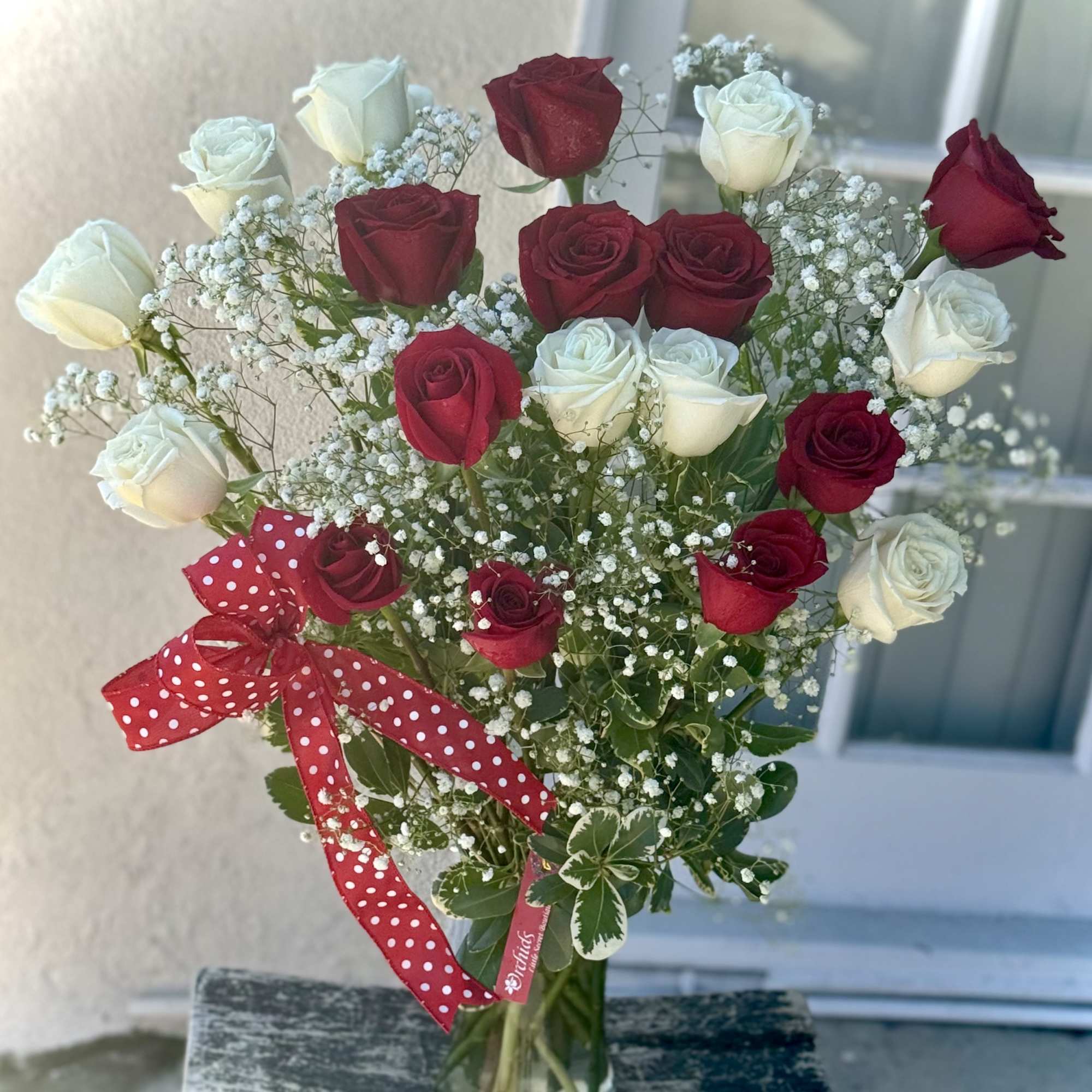 Bouquet of red and white roses in a clear glass vase with a red polka-dot ribbon