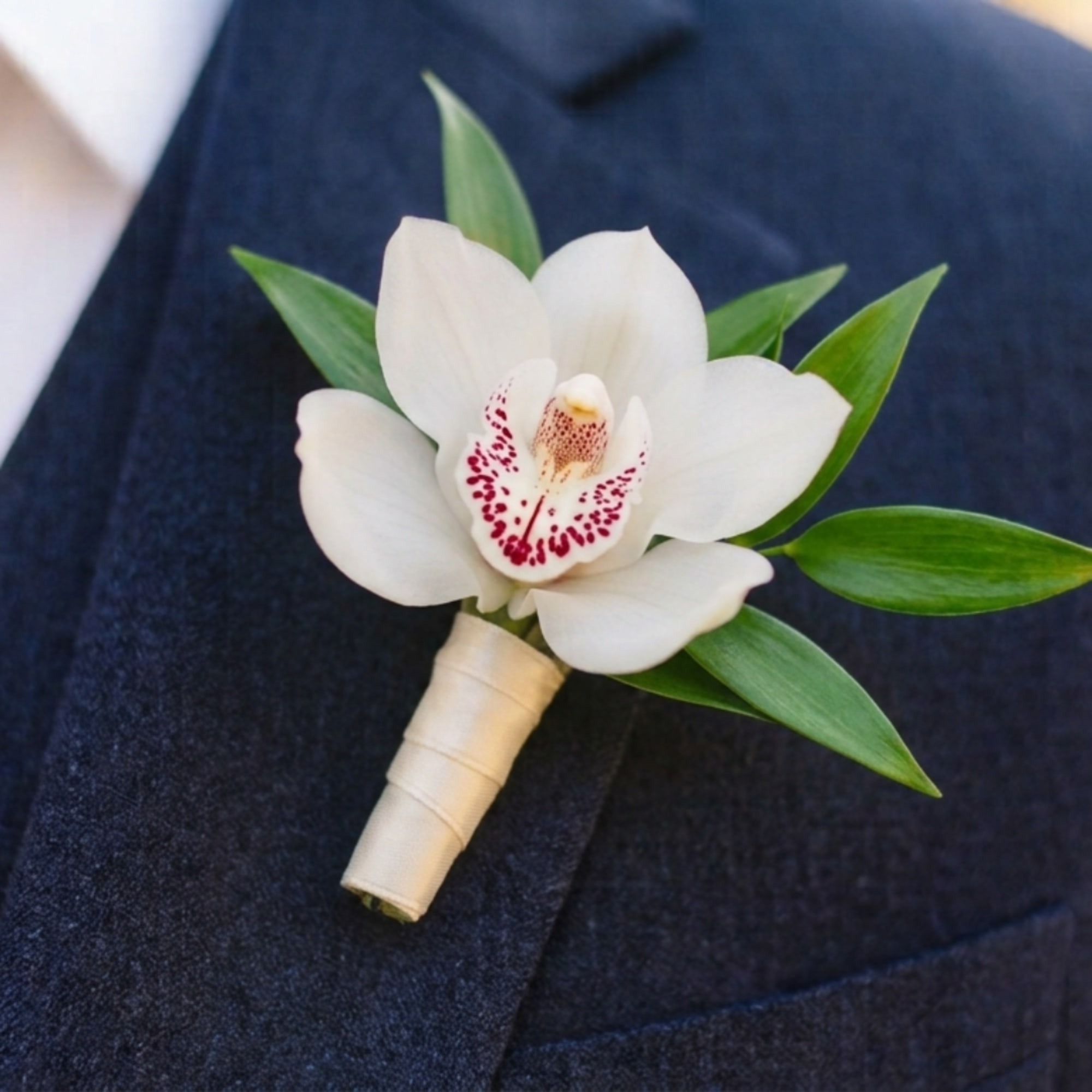 White orchid boutonniere with green leaves on a dark suit lapel