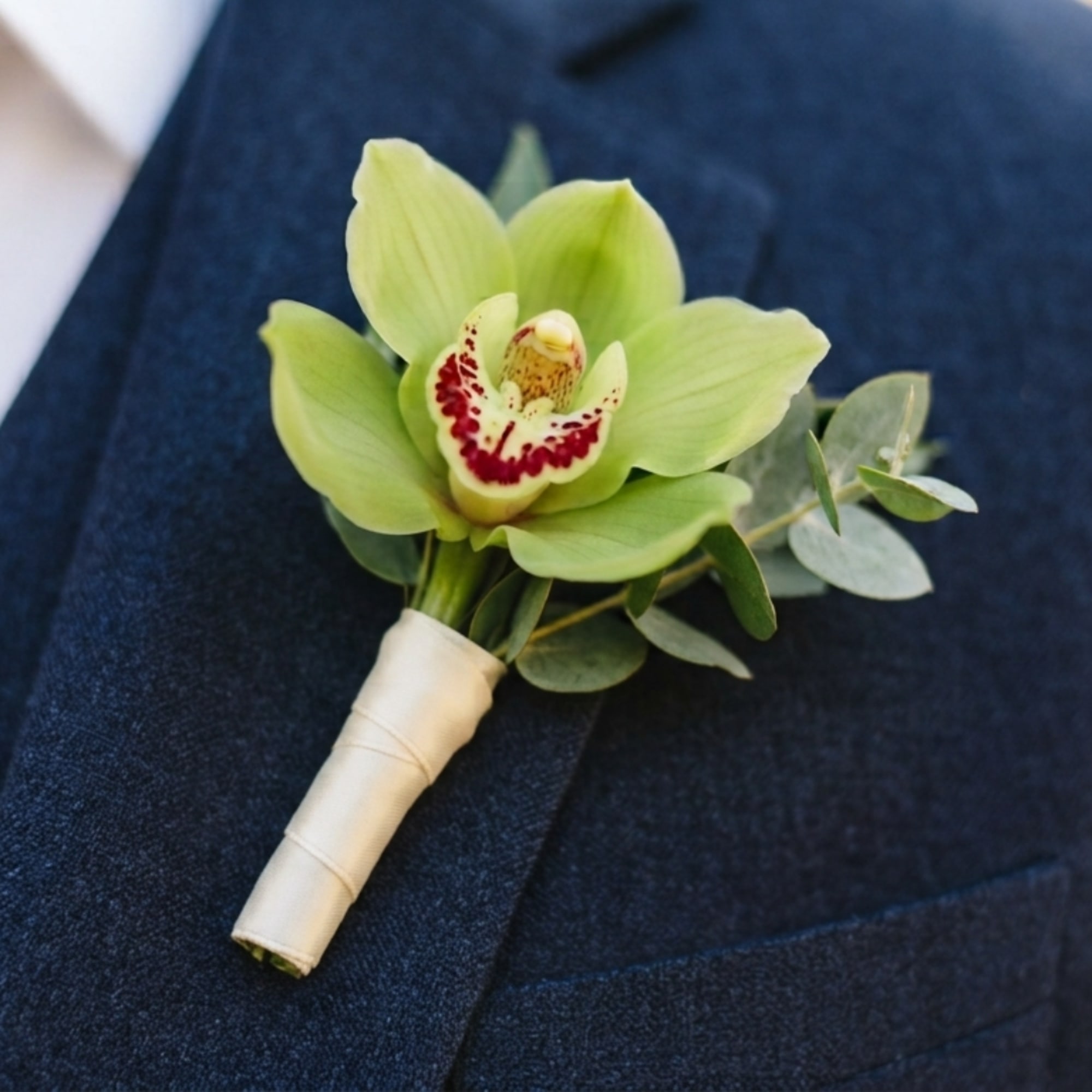 Green orchid boutonniere with eucalyptus on a dark jacket