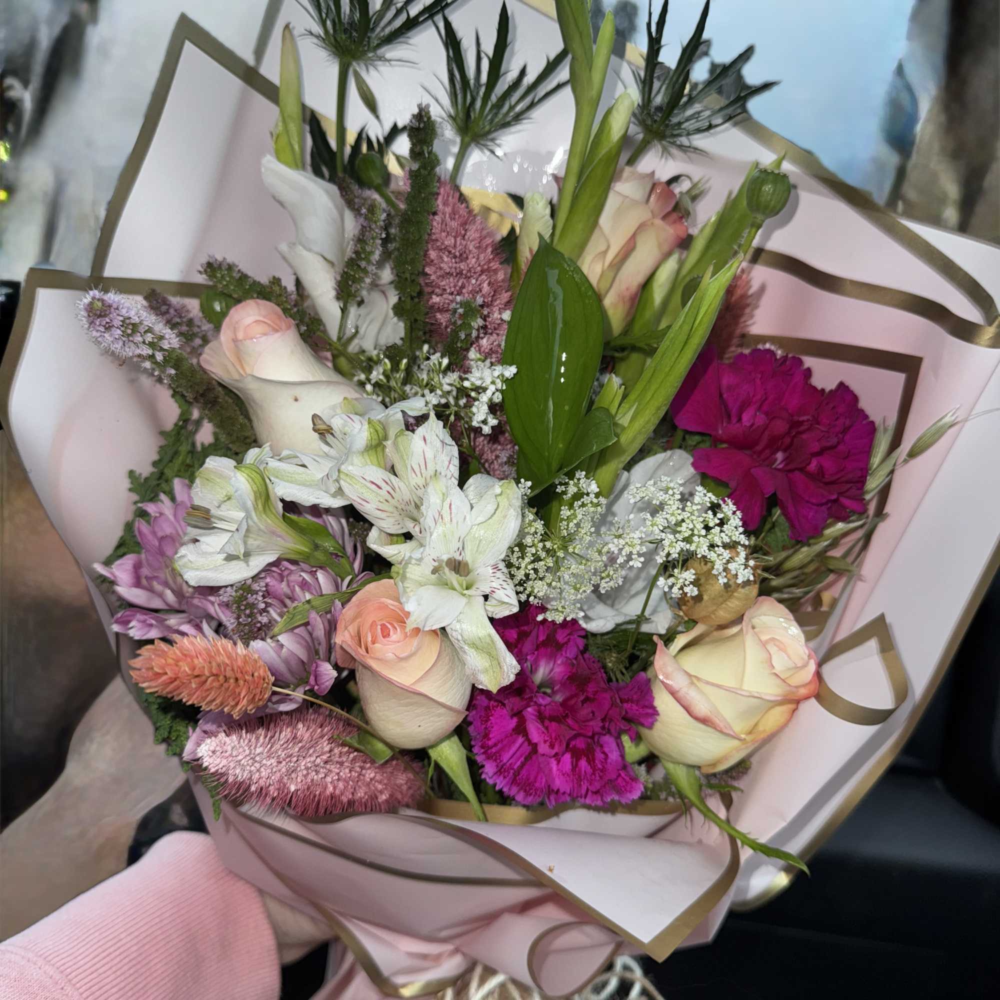 Hand-tied bouquet of pink, white, and magenta flowers wrapped in blush paper