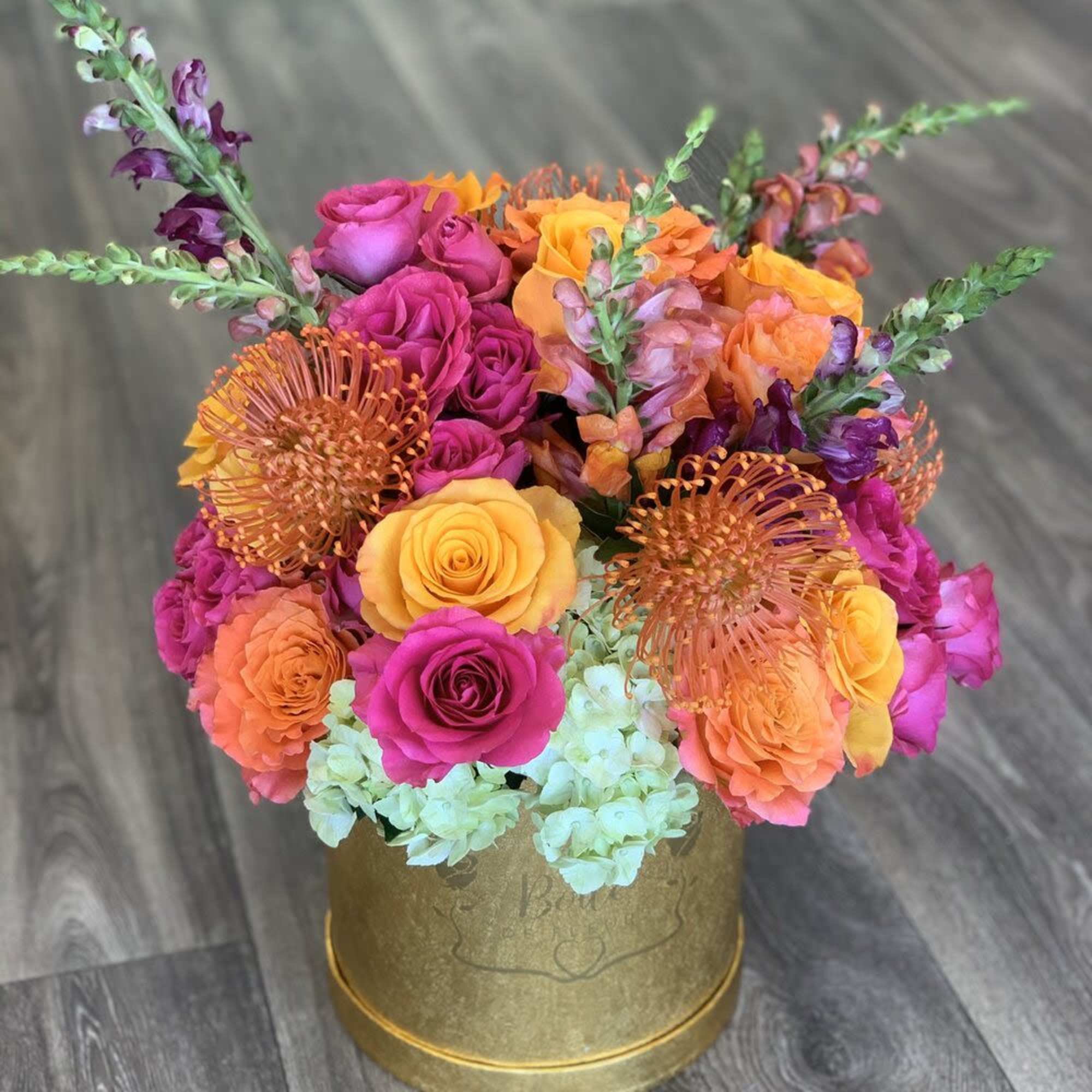 Bright bouquet of pink, orange, and yellow roses in a gold box