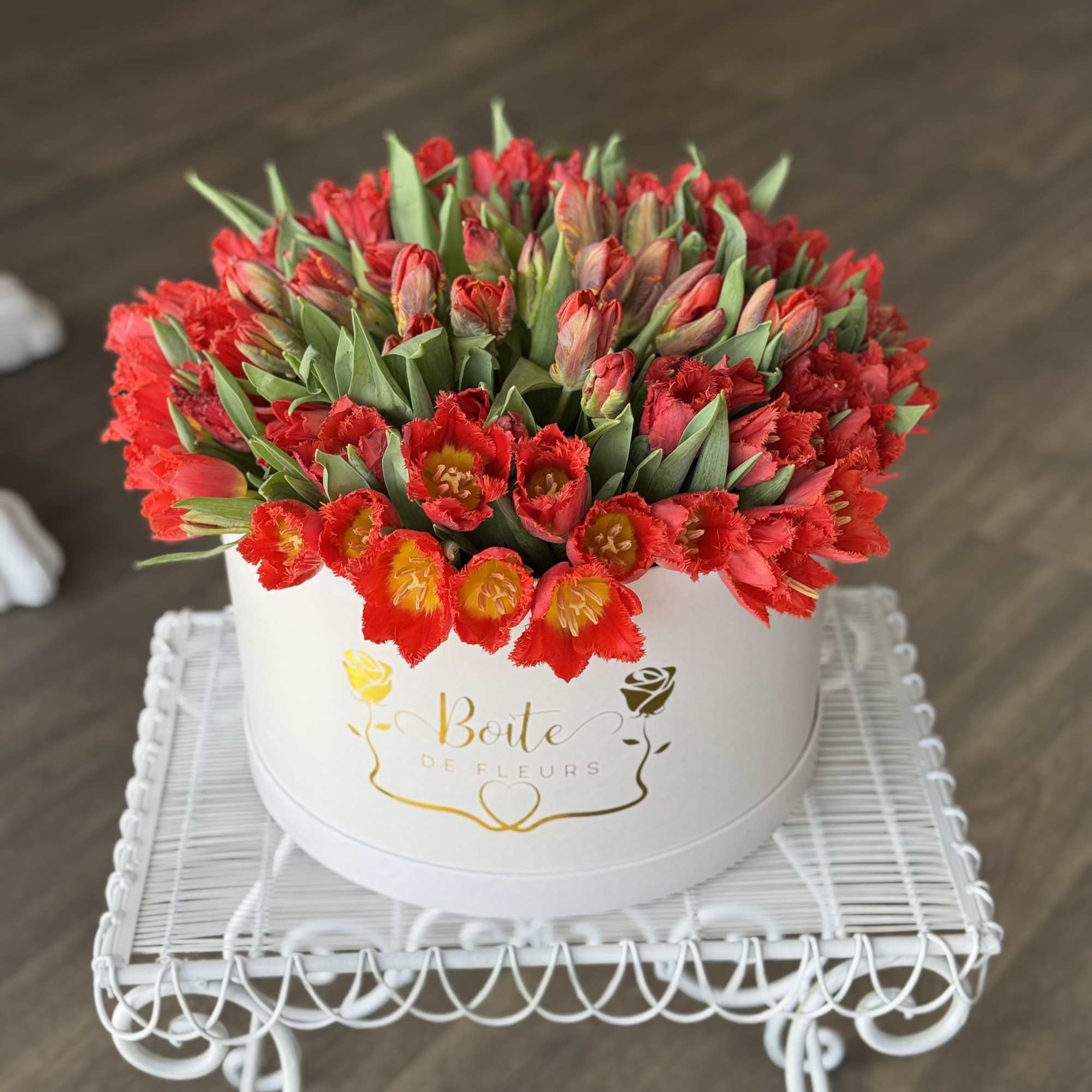 Round box filled with red tulips on a white stand