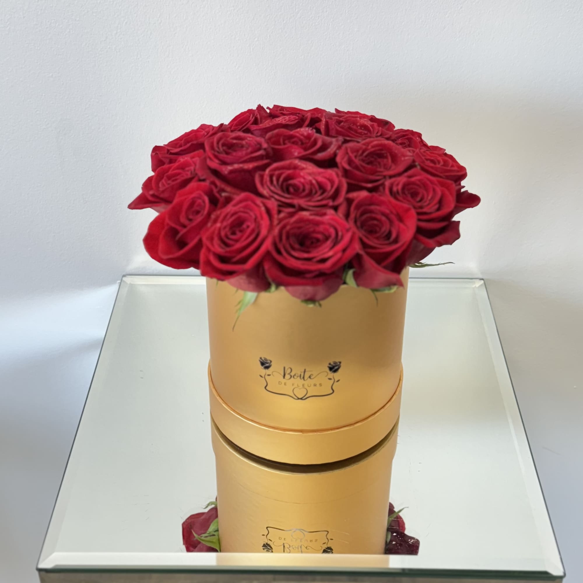 Red roses arranged in a gold round box on a mirrored table