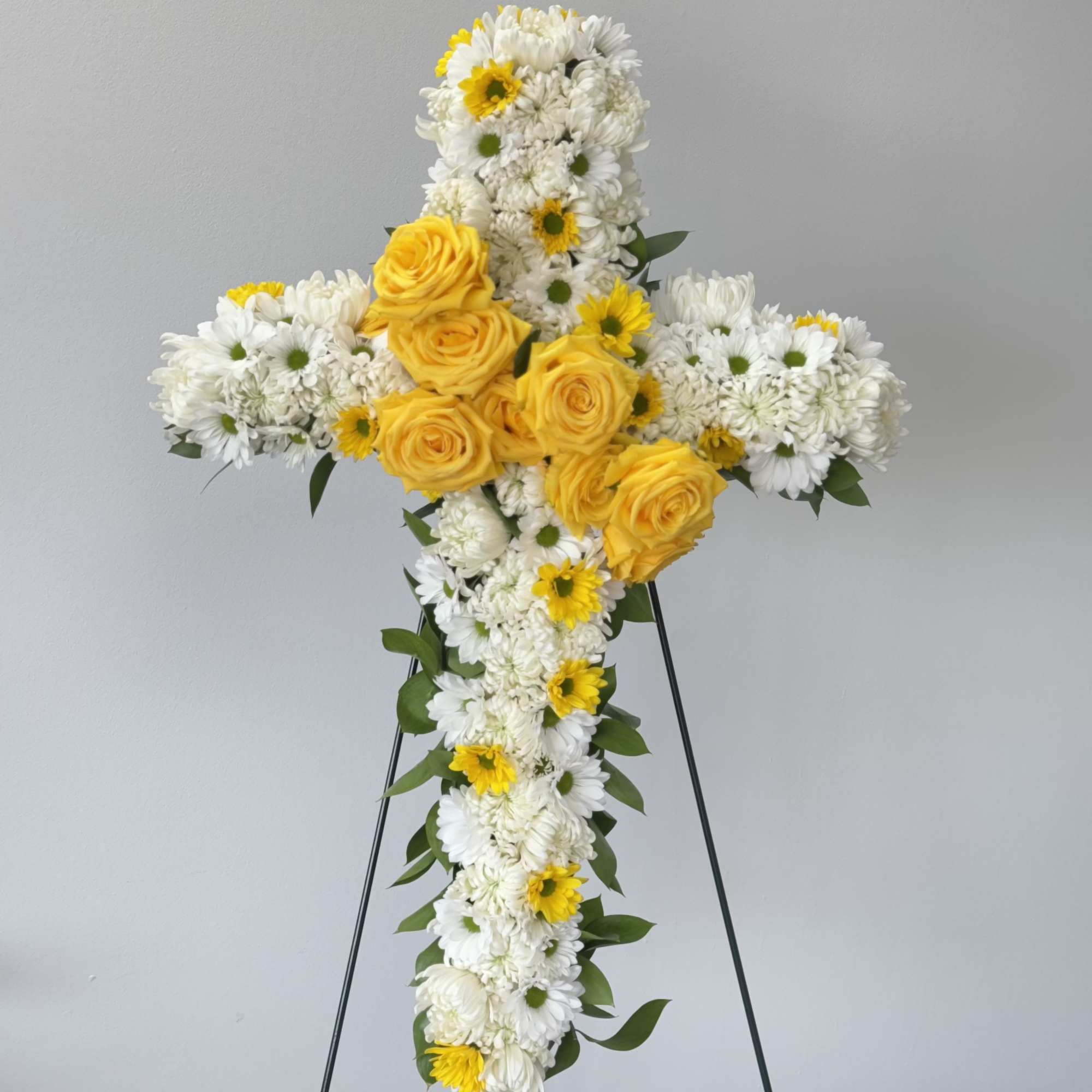 Yellow roses and white daisies arranged in a cross on a stand