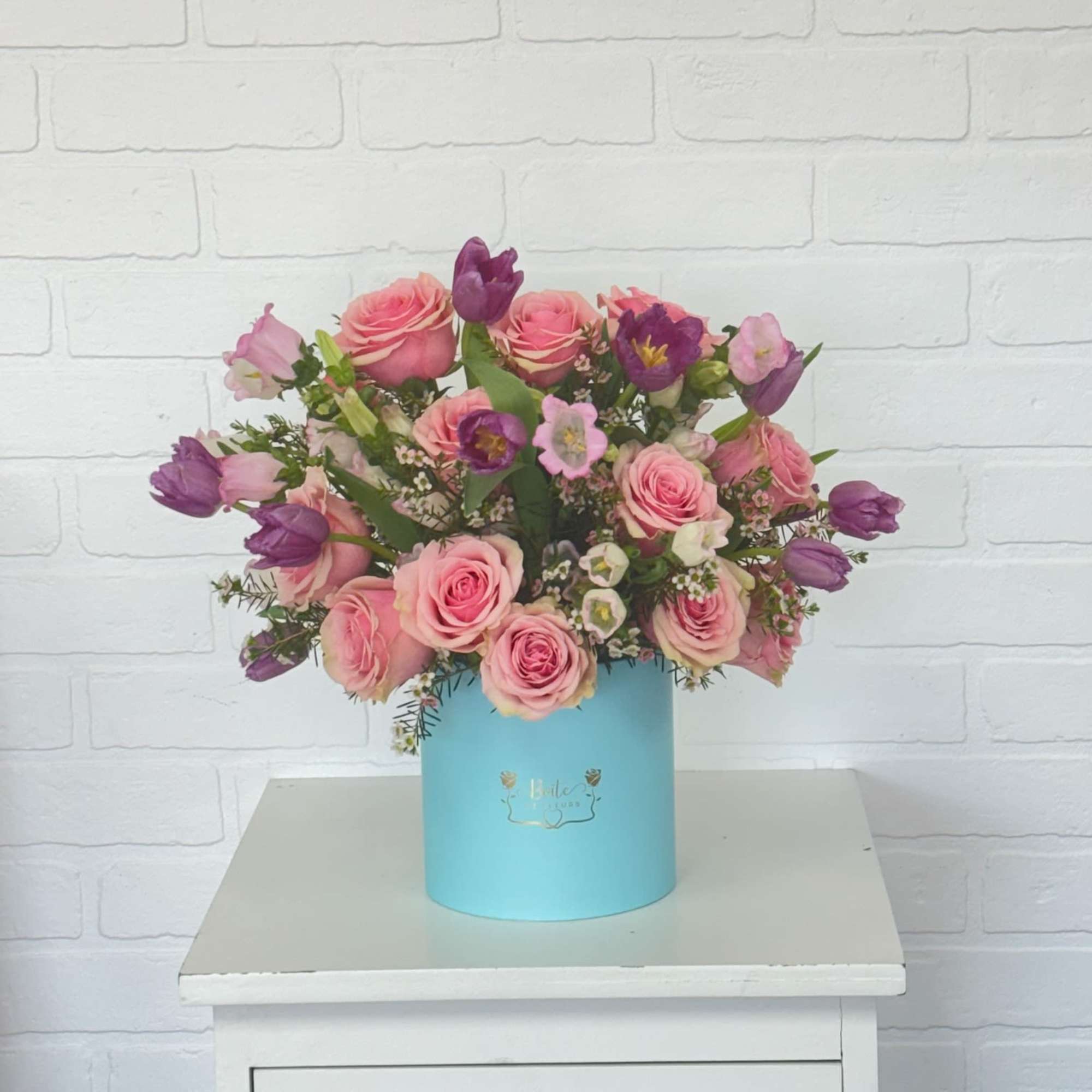 Pink and purple flower arrangement in a blue hat box