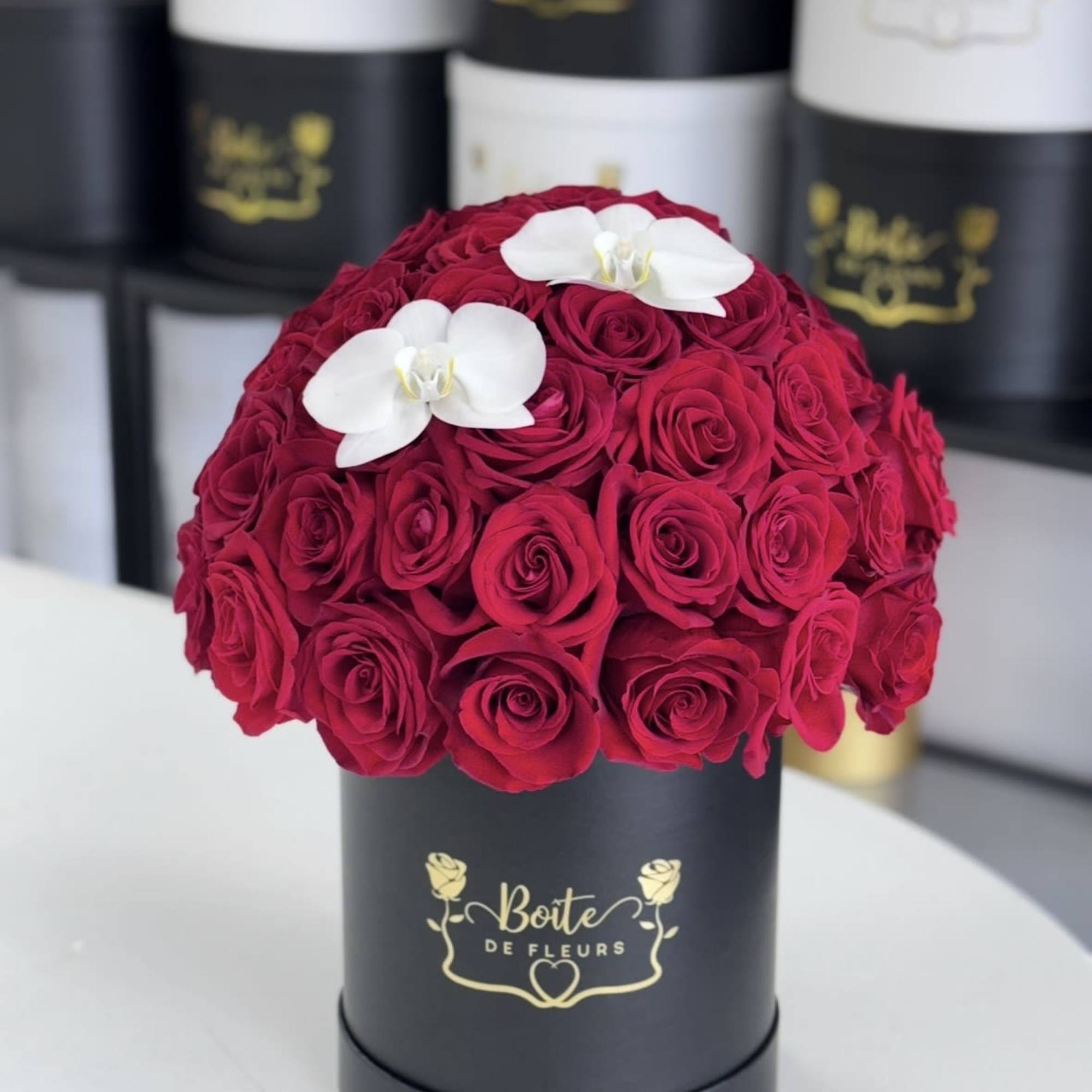 Round box of red roses topped with two white orchids