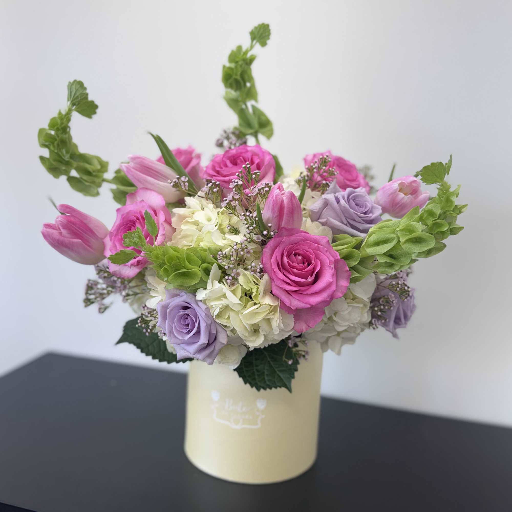 Pink and lavender roses with tulips in a cream vase