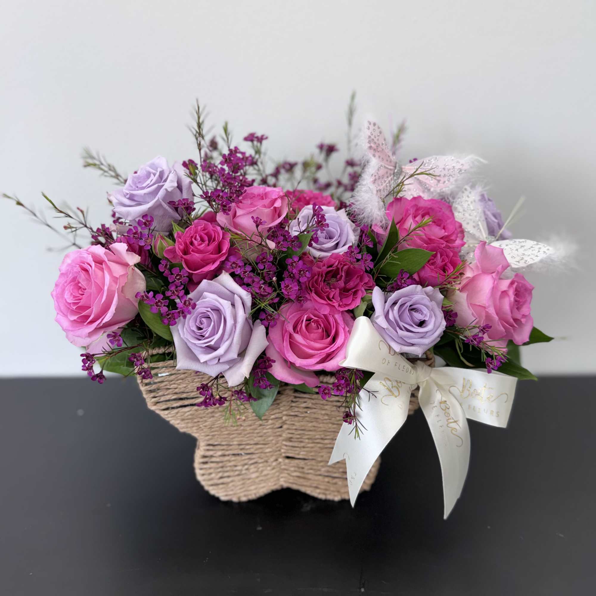 Pink and lavender roses arranged in a woven basket with a ribbon bow