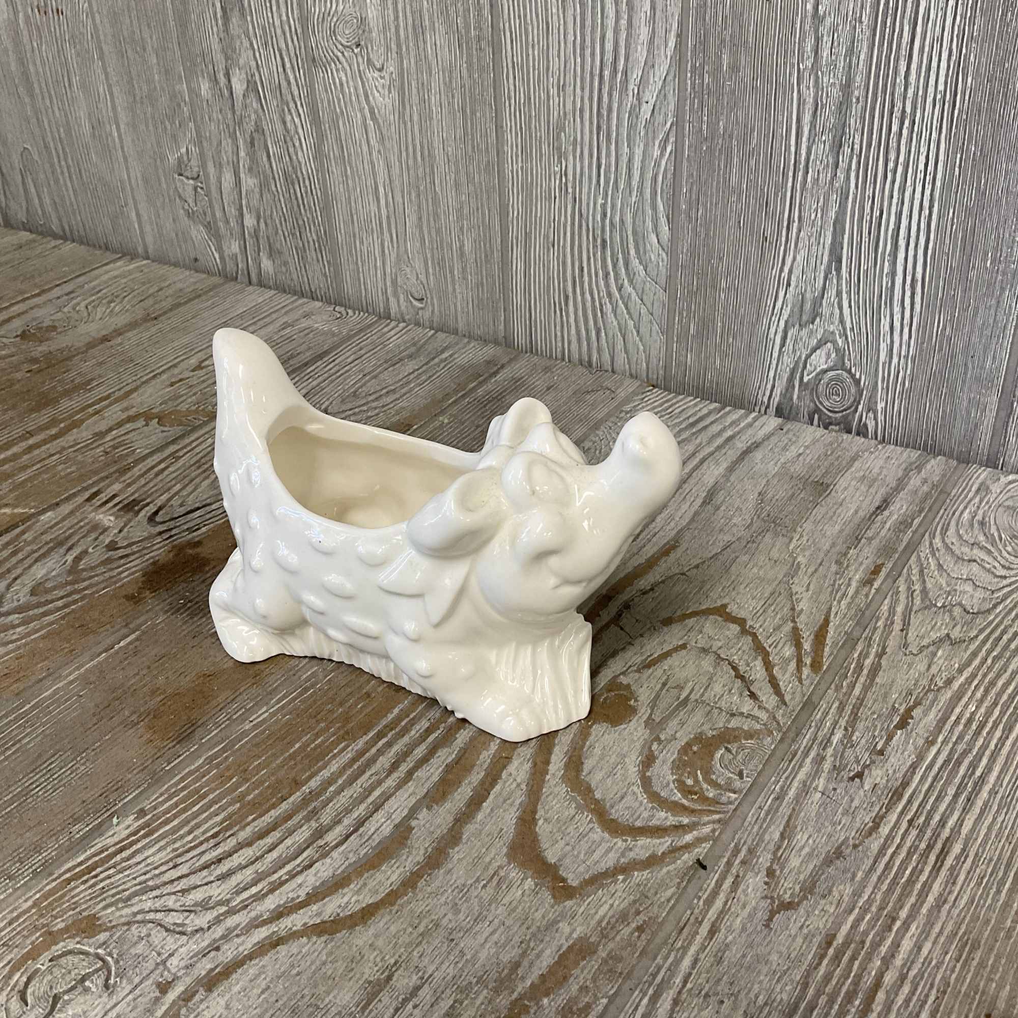 White ceramic cow-shaped planter on a wood surface