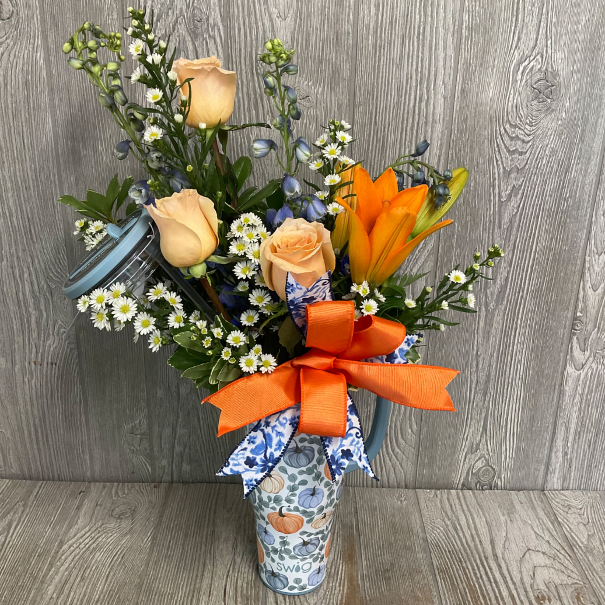 Mixed bouquet with peach roses, orange lilies, and small white daisies in a patterned tumbler
