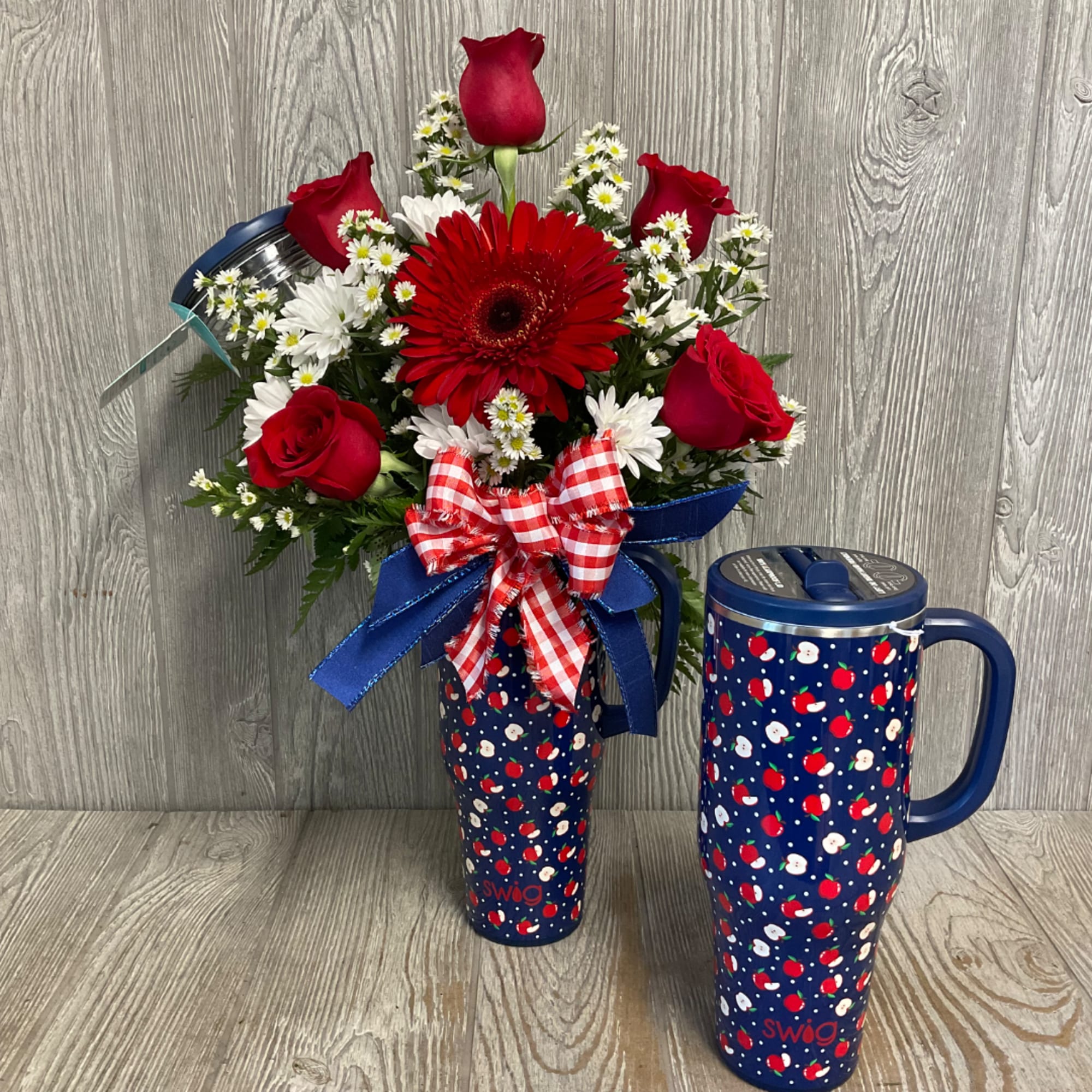 Red roses and white daisies in a patterned travel tumbler with a ribbon bow