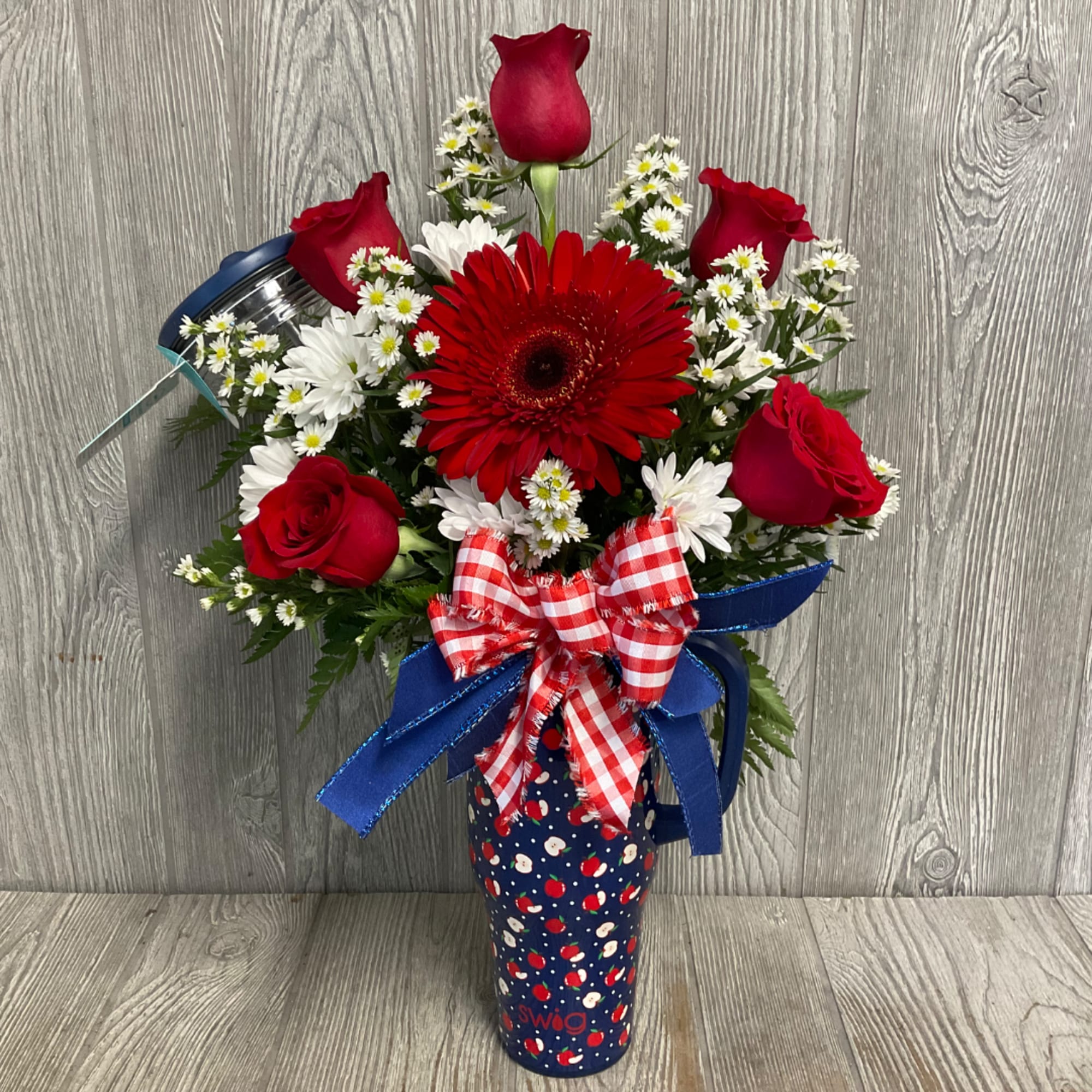Red roses and daisies arranged in a patterned tumbler with a ribbon bow