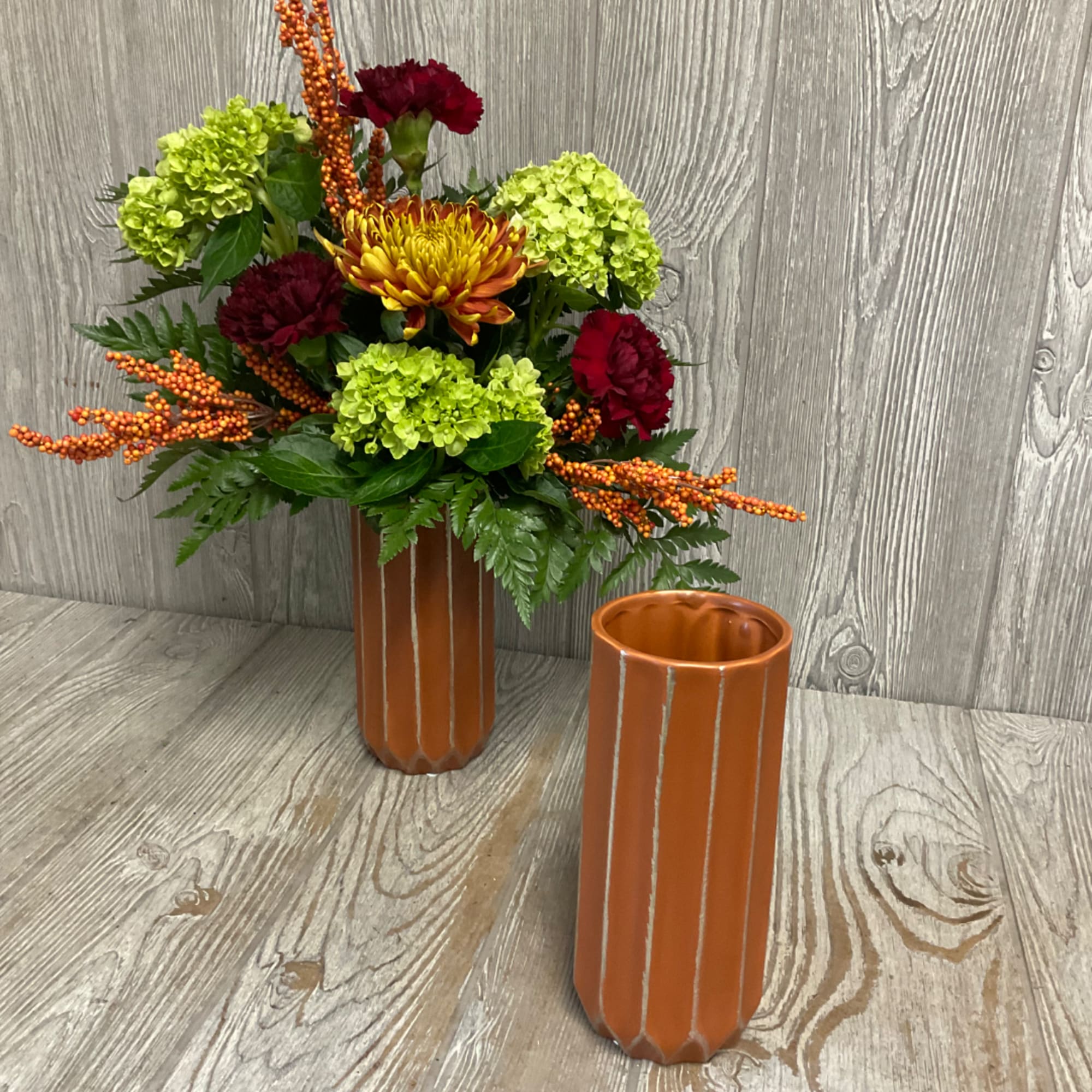 Colorful floral arrangement in a tall orange vase beside a matching empty vase