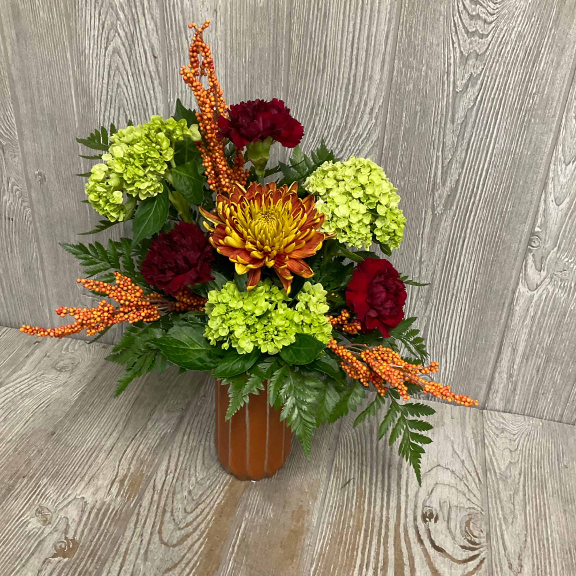 Mixed floral arrangement in a brown vase with green hydrangeas and red carnations