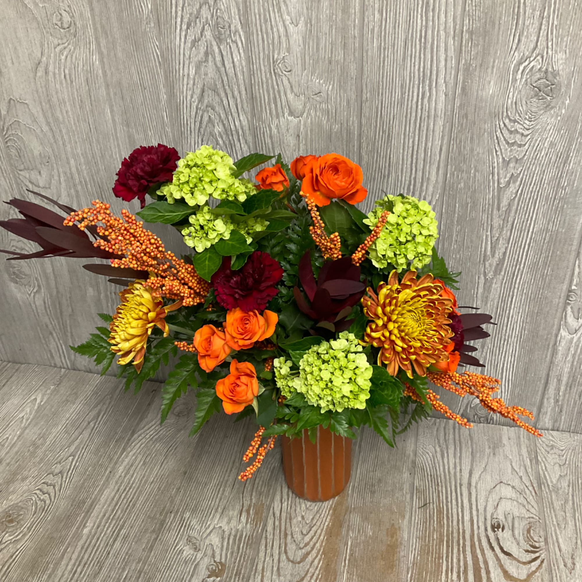 Orange roses and chrysanthemums arranged with green hydrangeas in a vase