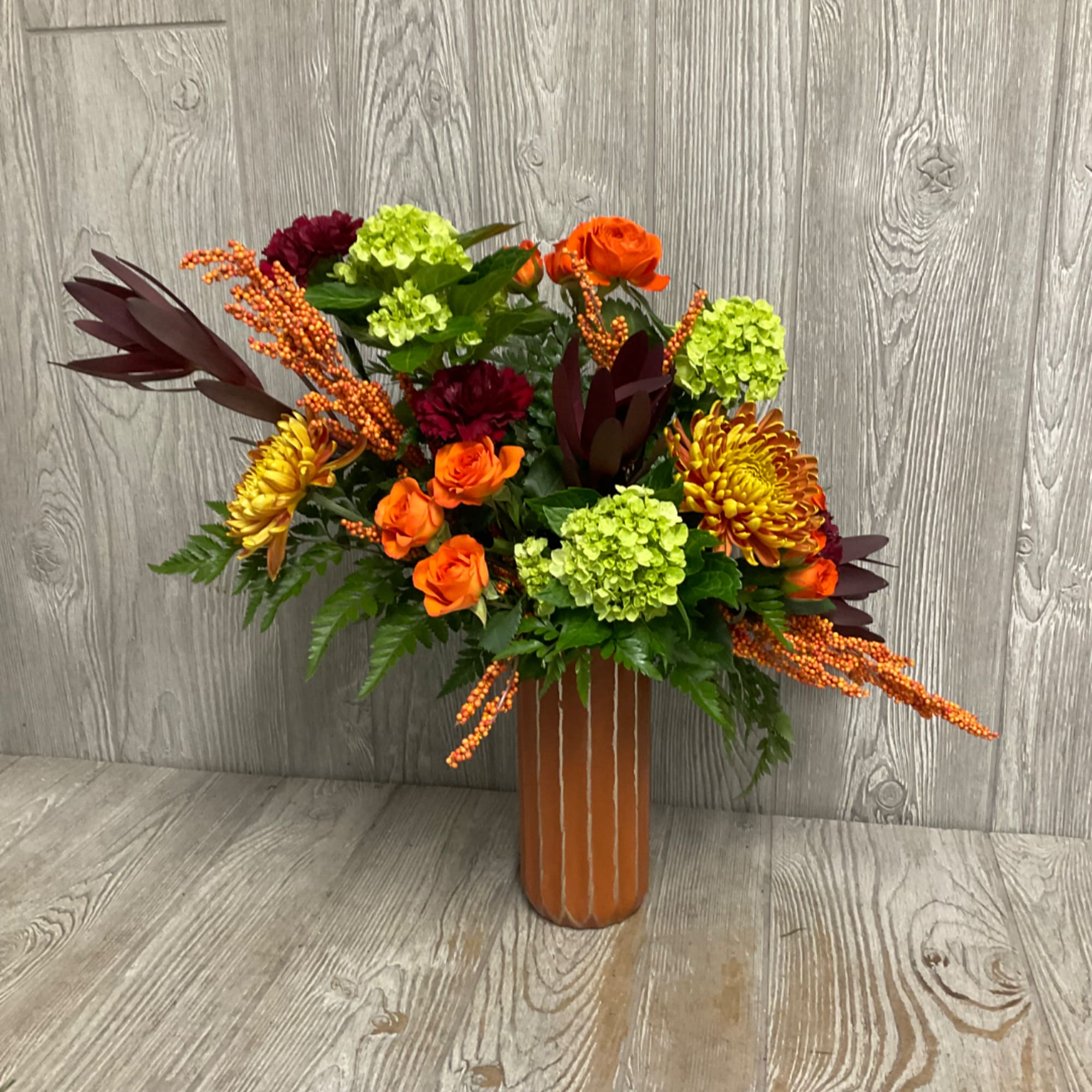 Orange and burgundy floral arrangement in a tall vase