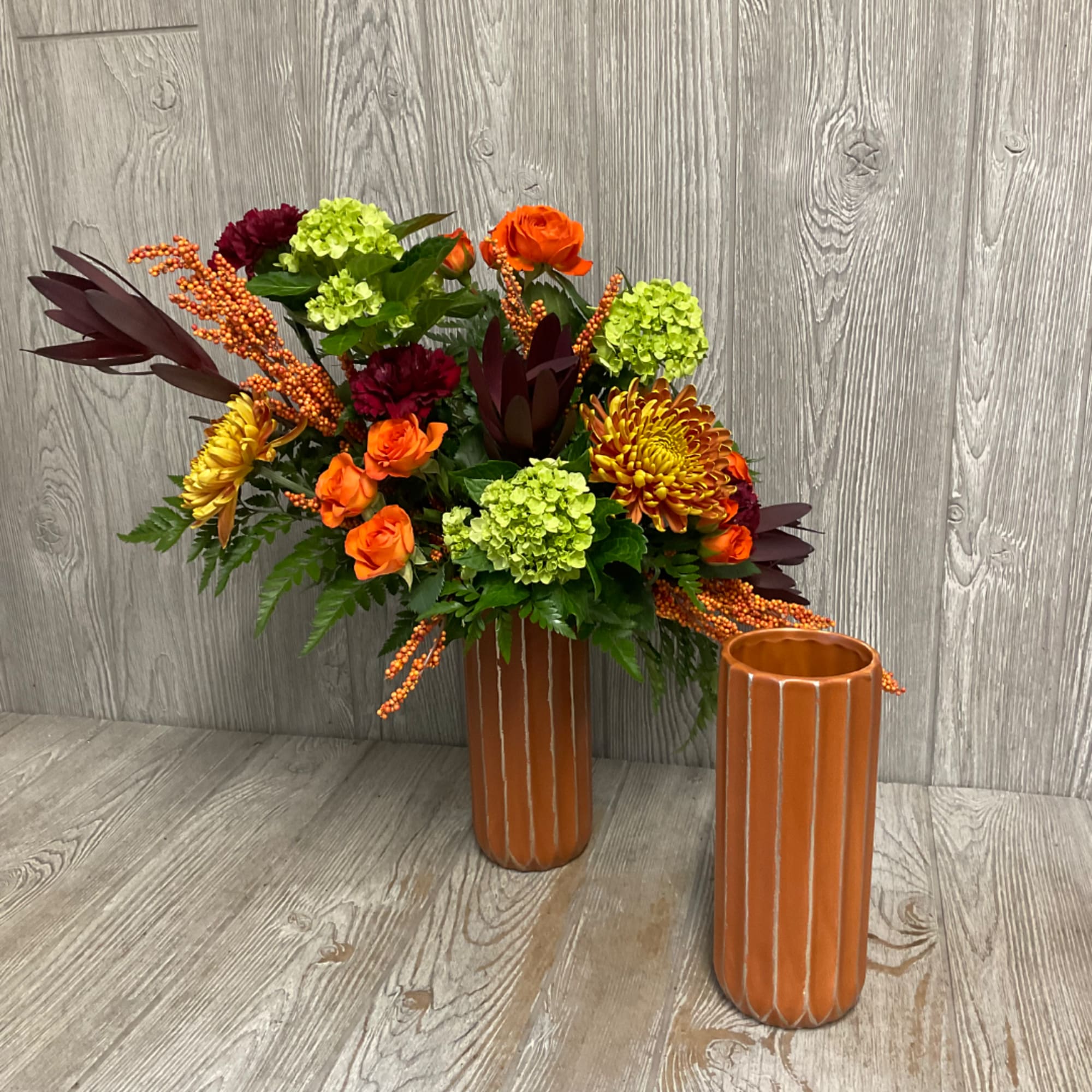 Orange and burgundy floral arrangement in a ribbed ceramic vase