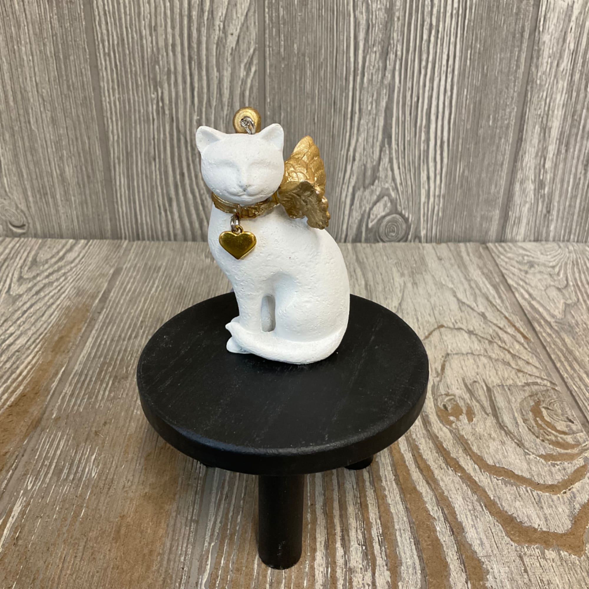 White cat figurine with gold wings and heart charm on a black stand