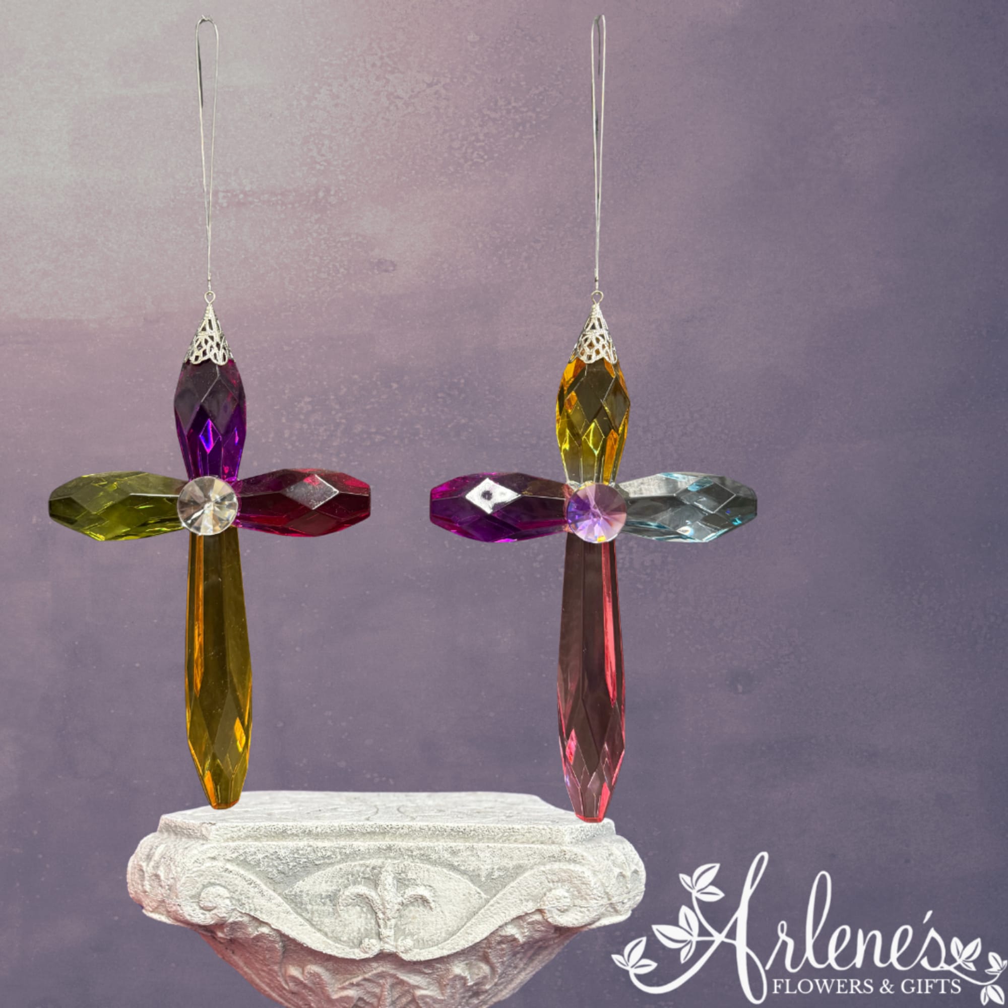 Two colorful crystal cross ornaments hang above a carved pedestal