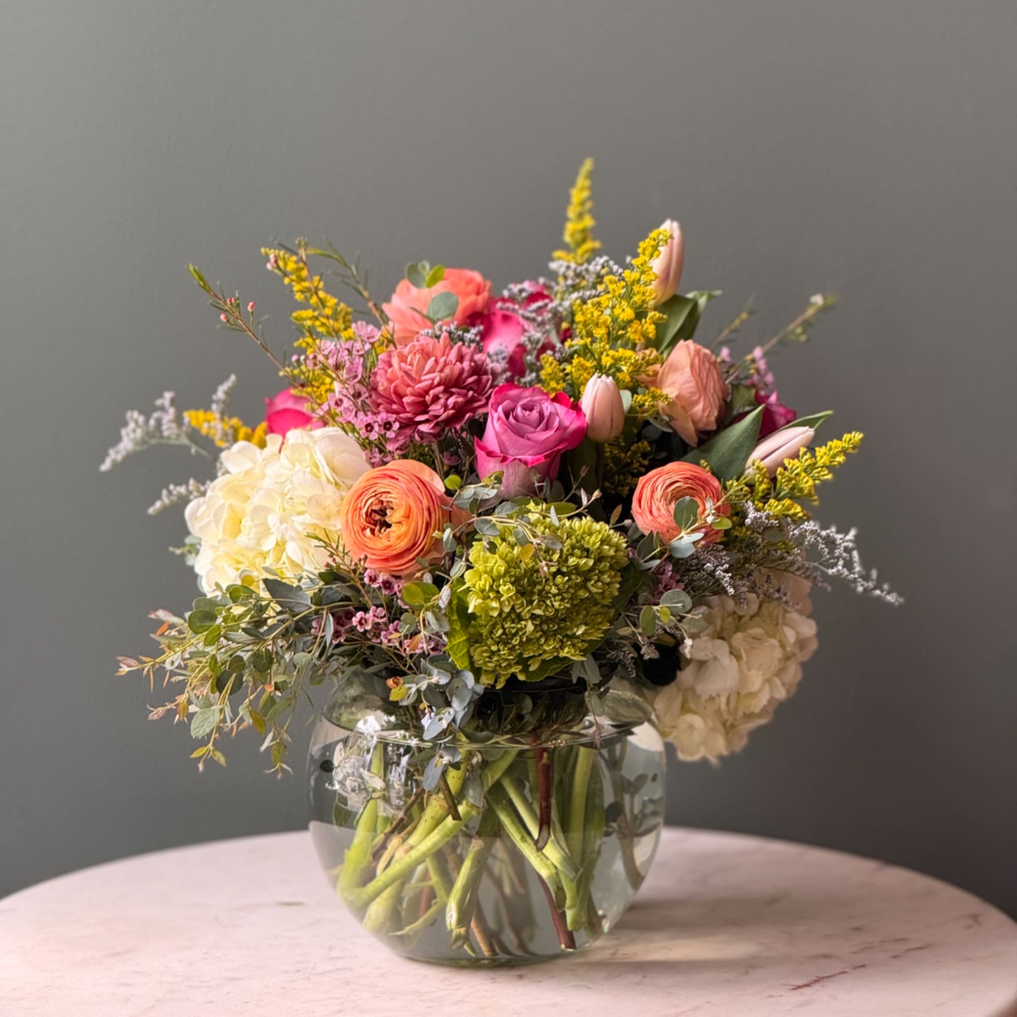 Mixed bouquet in a clear glass vase with pink, peach, white, and yellow blooms