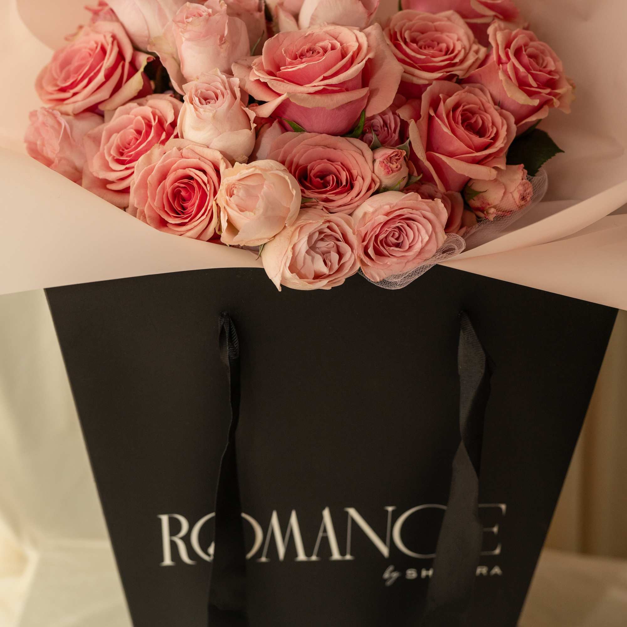 Bouquet of pink roses wrapped in pale paper and a black gift bag