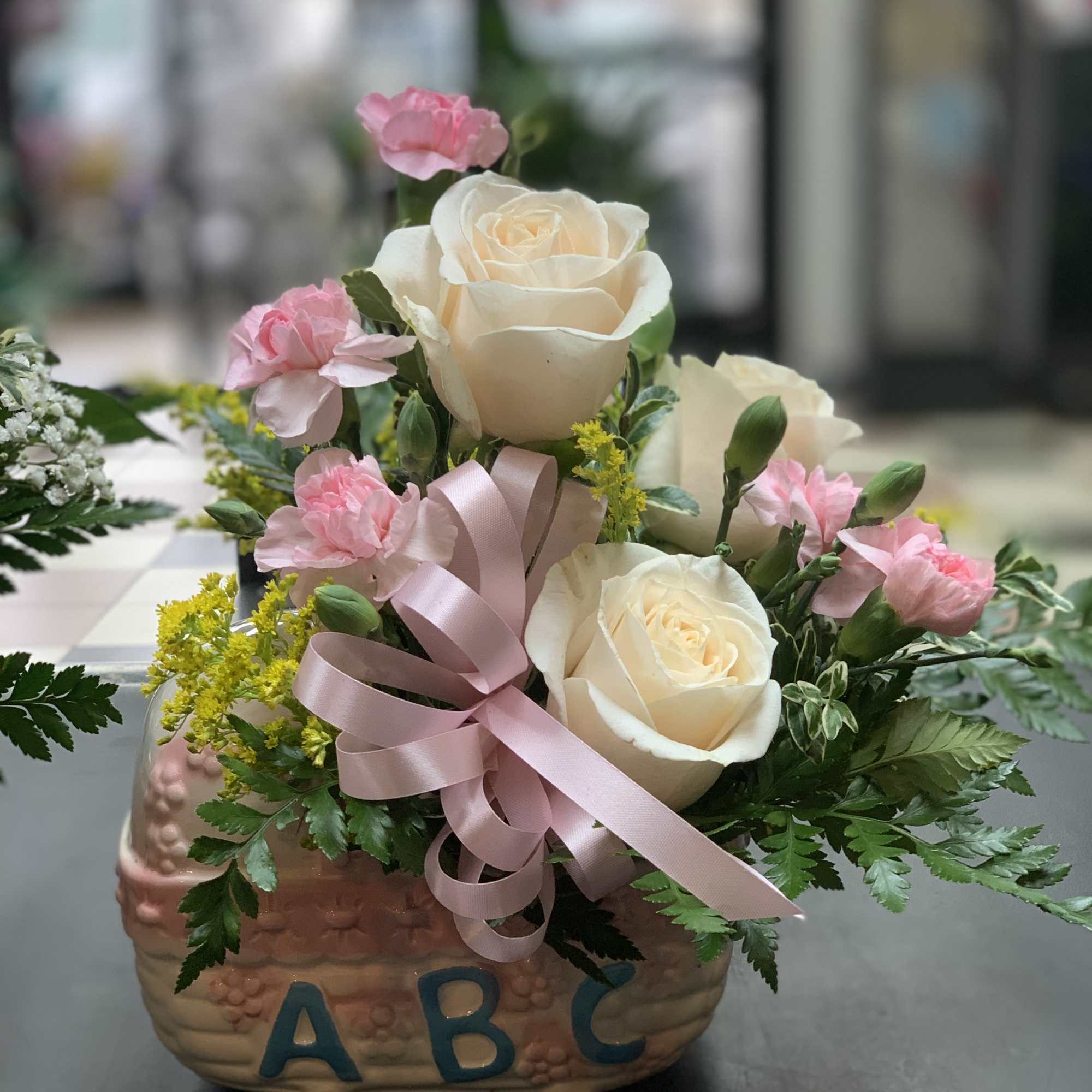 Pink and white rose arrangement in a decorative ceramic container with a ribbon bow