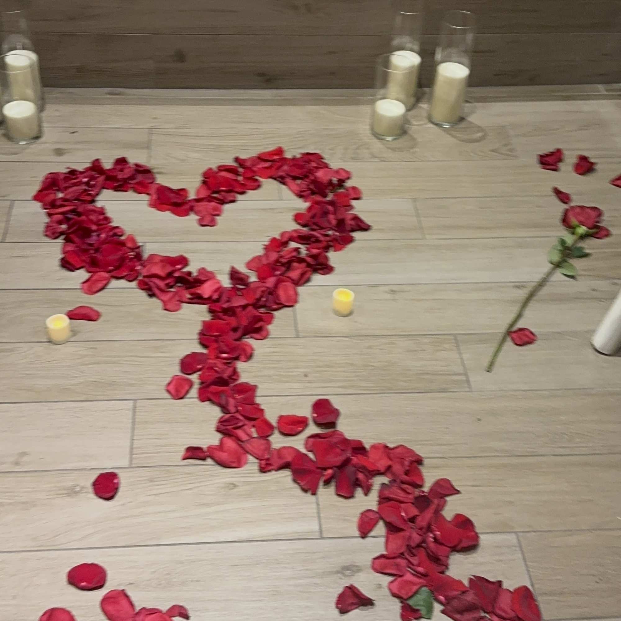 Rose petals arranged in a heart shape on the floor with candles nearby