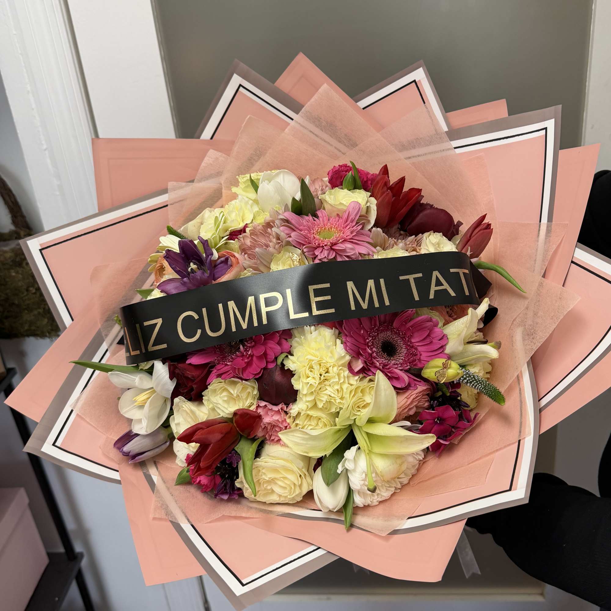 Mixed bouquet with pink, white, yellow, and red flowers wrapped in peach paper