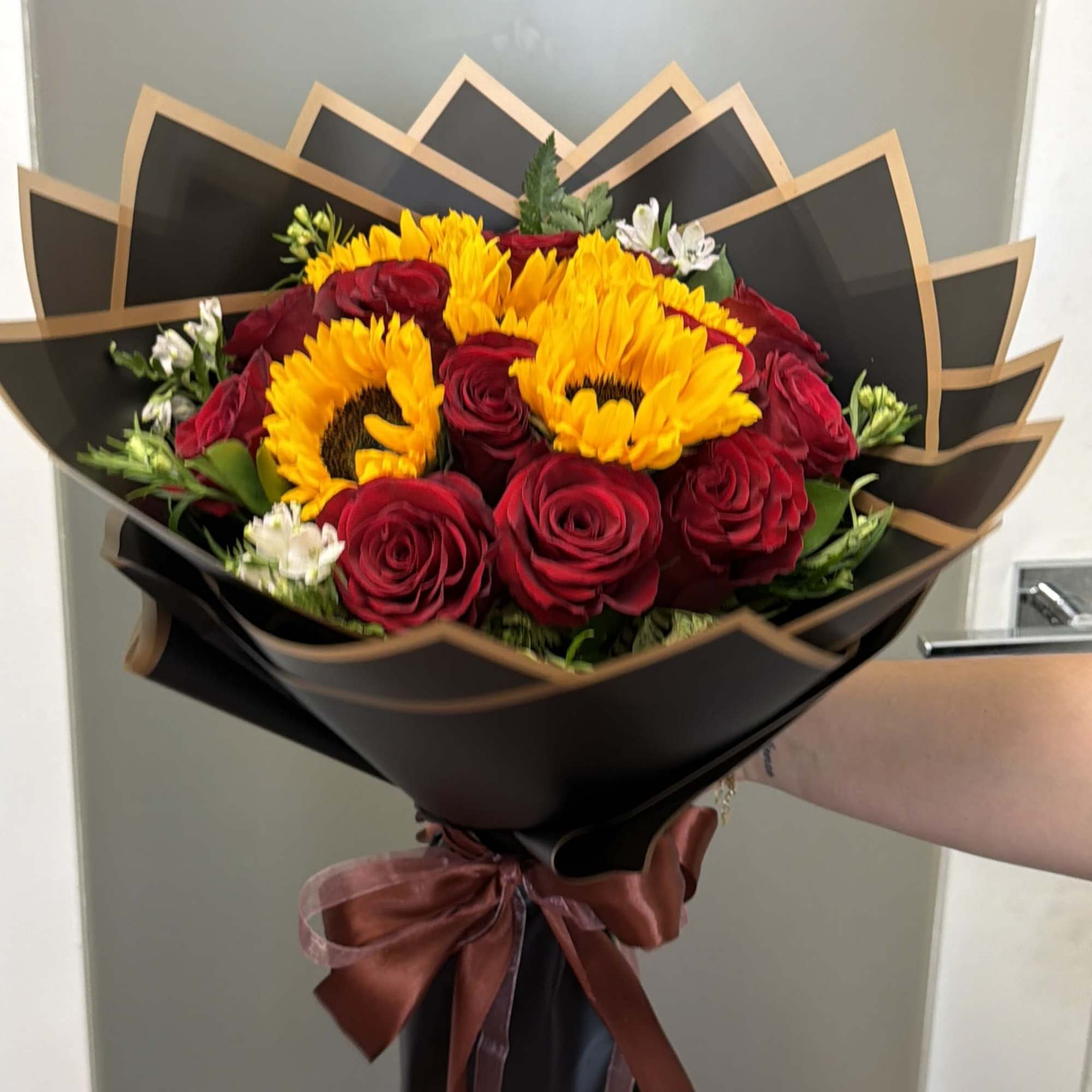 Bouquet of red roses and yellow sunflowers wrapped in black paper