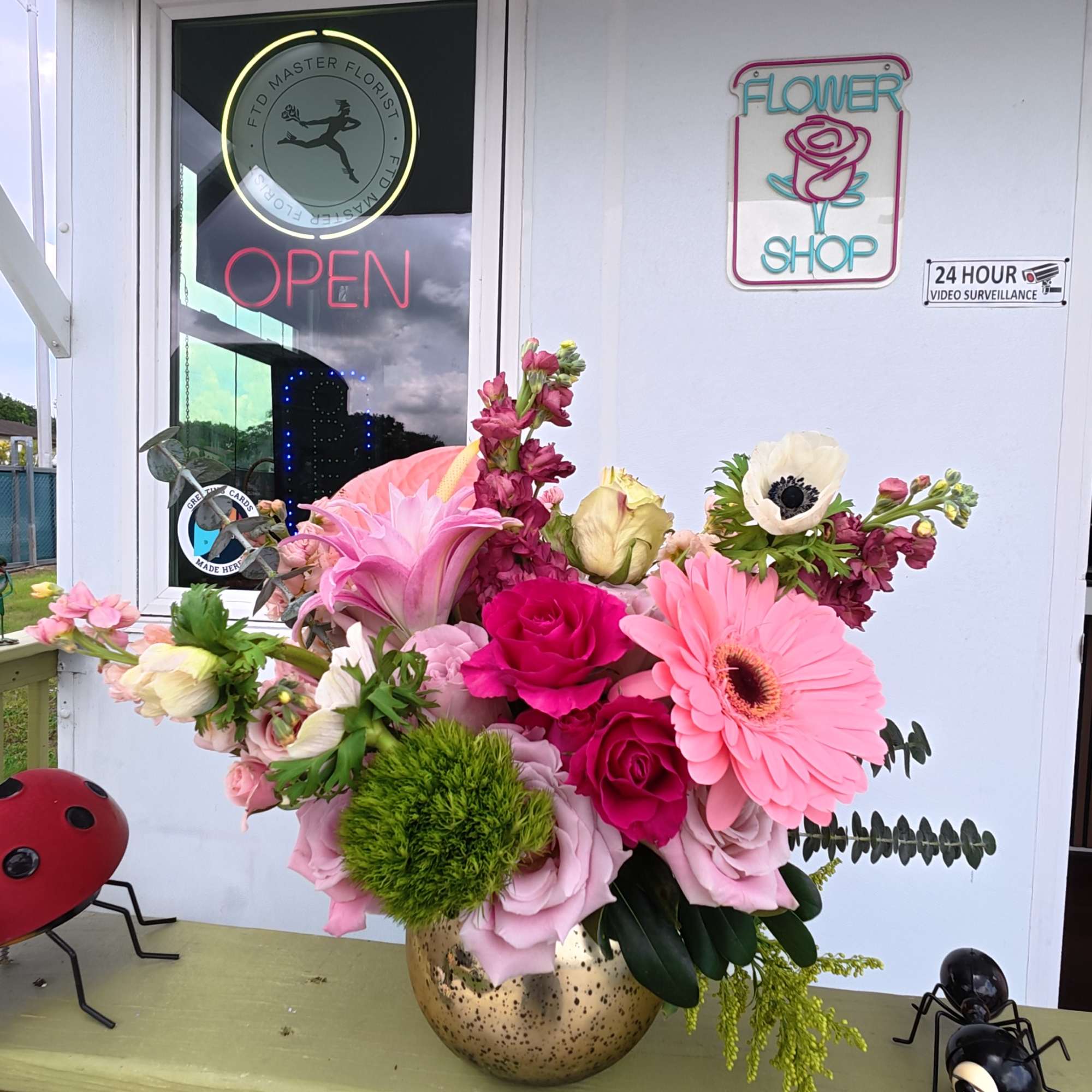 Pink and white floral arrangement in a gold vase on a porch