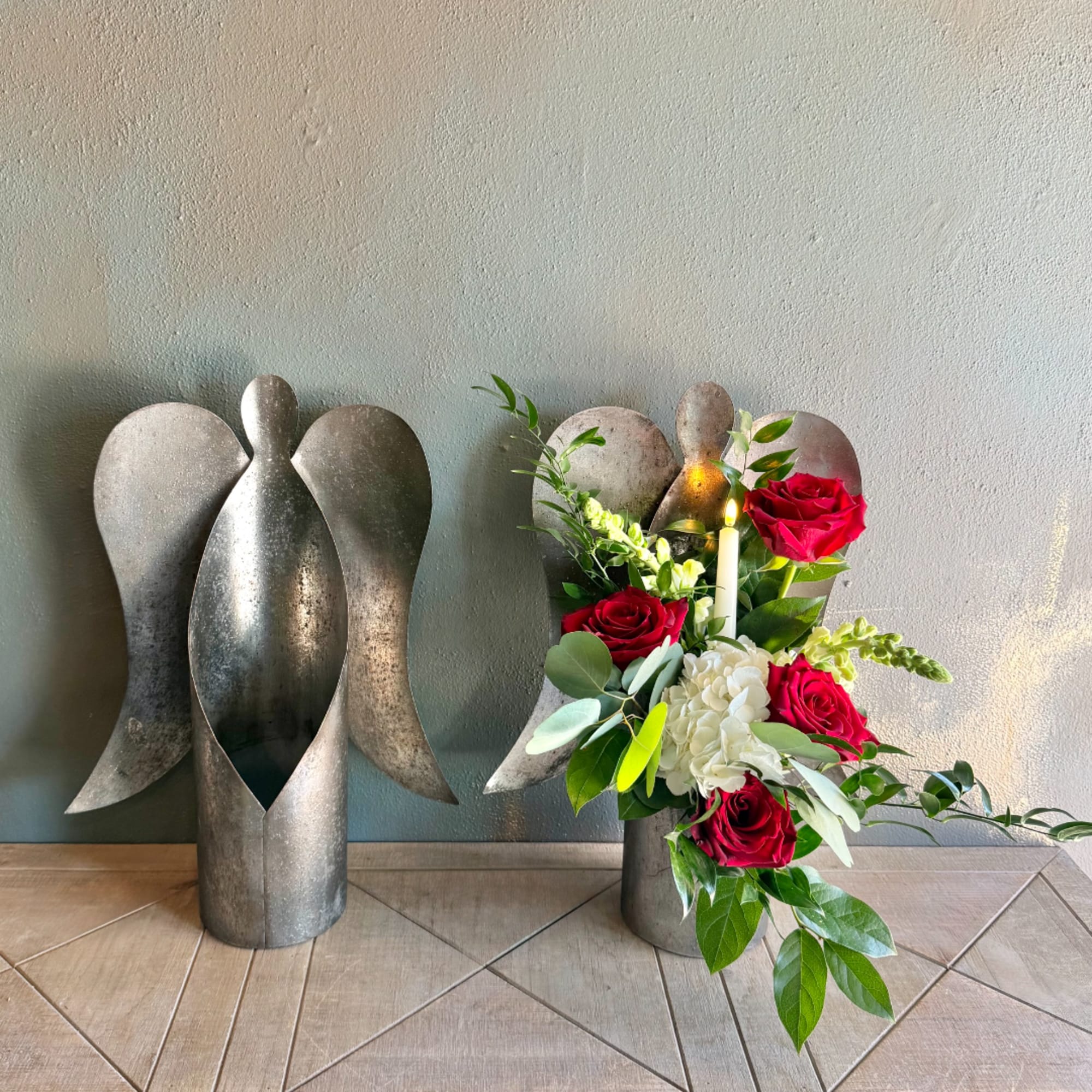 Red roses and white hydrangea arranged in a silver angel-shaped vase with a candle
