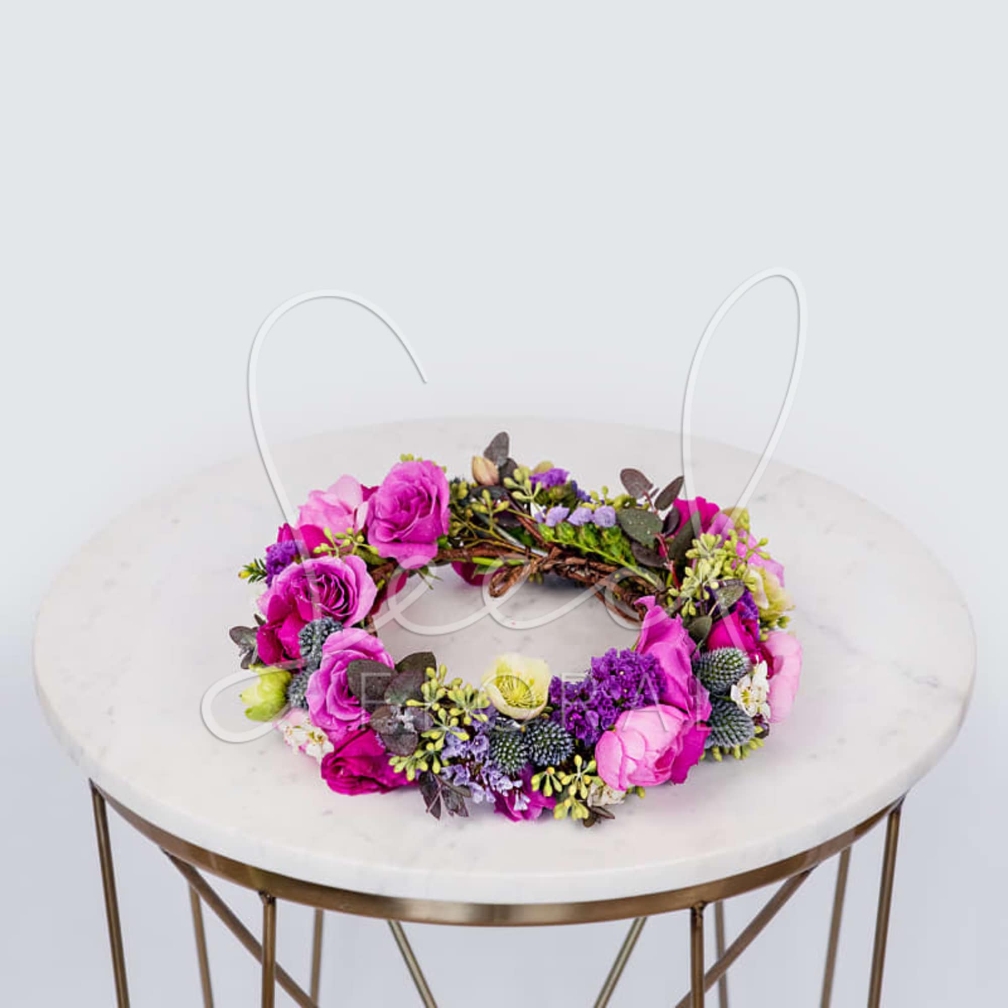 Bright pink and purple floral wreath with roses and mixed blooms on a round marble table.