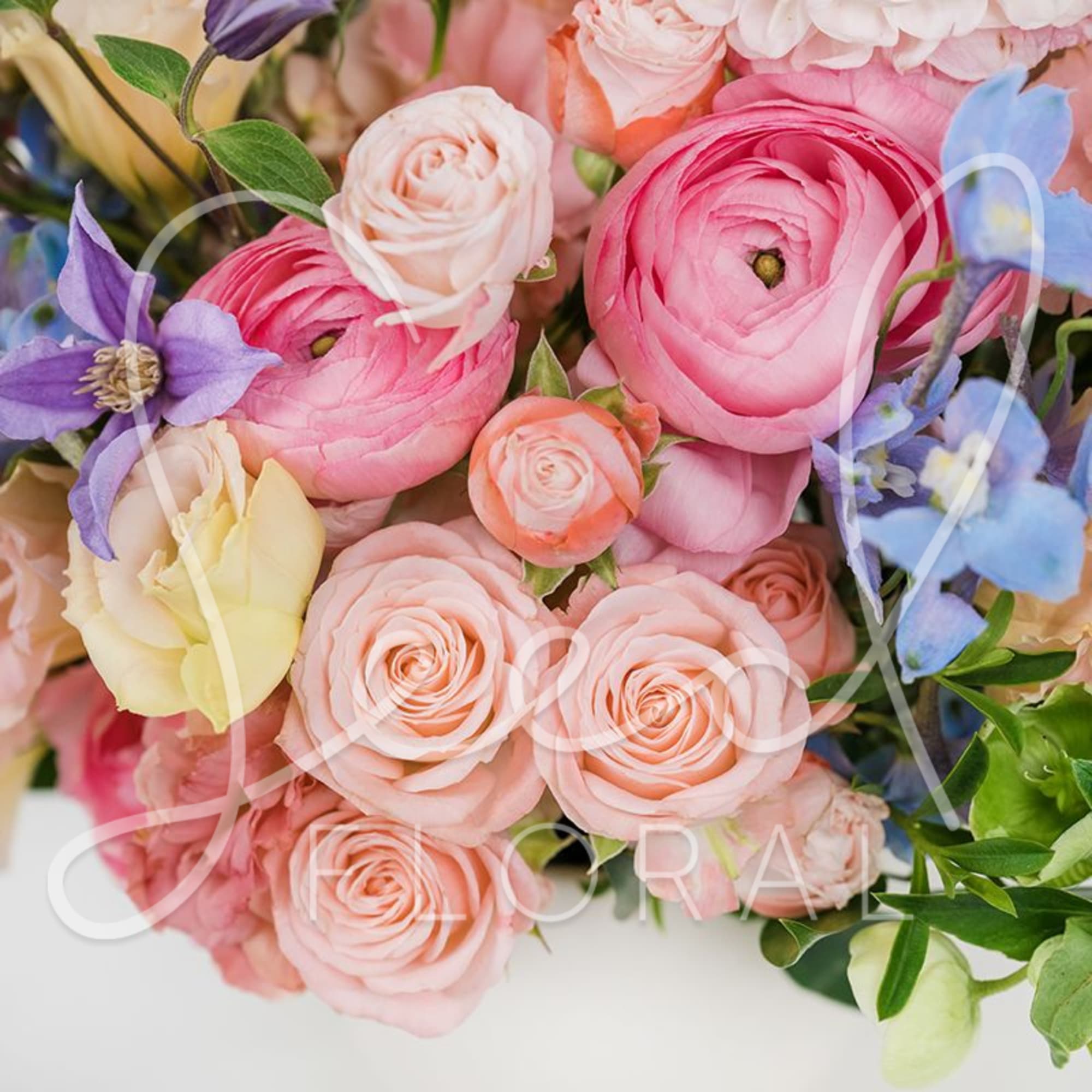 Close-up of pastel bouquet with pink ranunculus, peach roses, and blue and purple accent flowers.